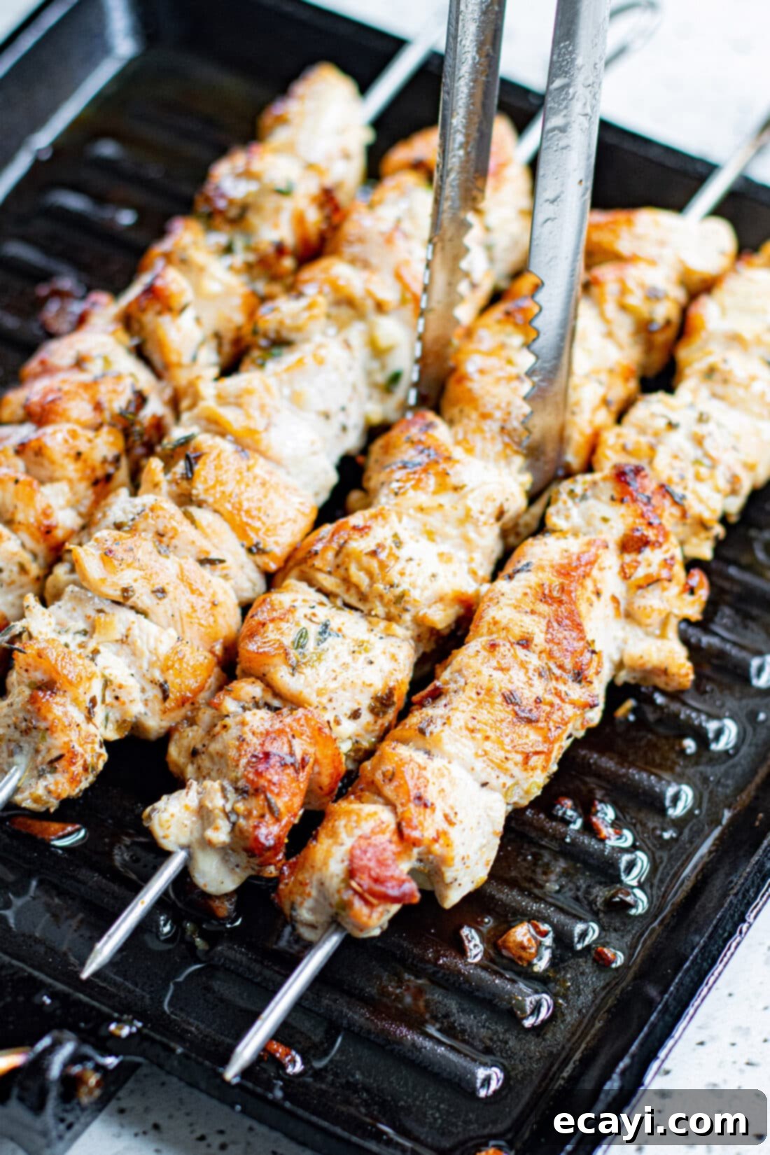 Lemon-Herb Mediterranean Chicken Skewers 9 Tongs lifting a perfectly grilled Greek Chicken Kabob off the grill