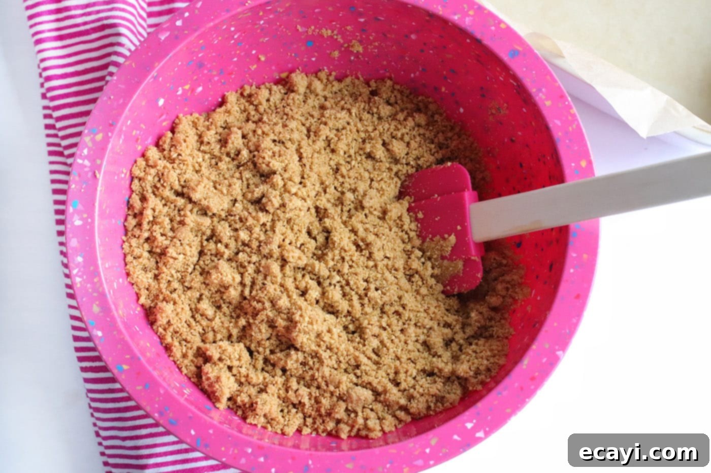 Effortless Strawberry Cheesecake Bars 5 graham cracker crumbs mixed with butter and water in a bowl with a rubber spatula