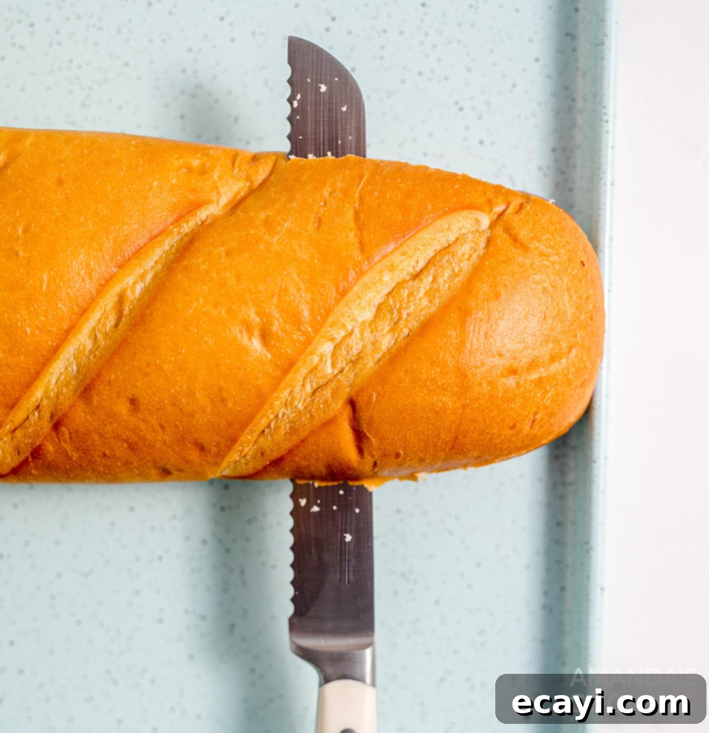 Garlic Cheese Bliss 5 A knife slicing a French bread loaf in half lengthwise on a cutting board
