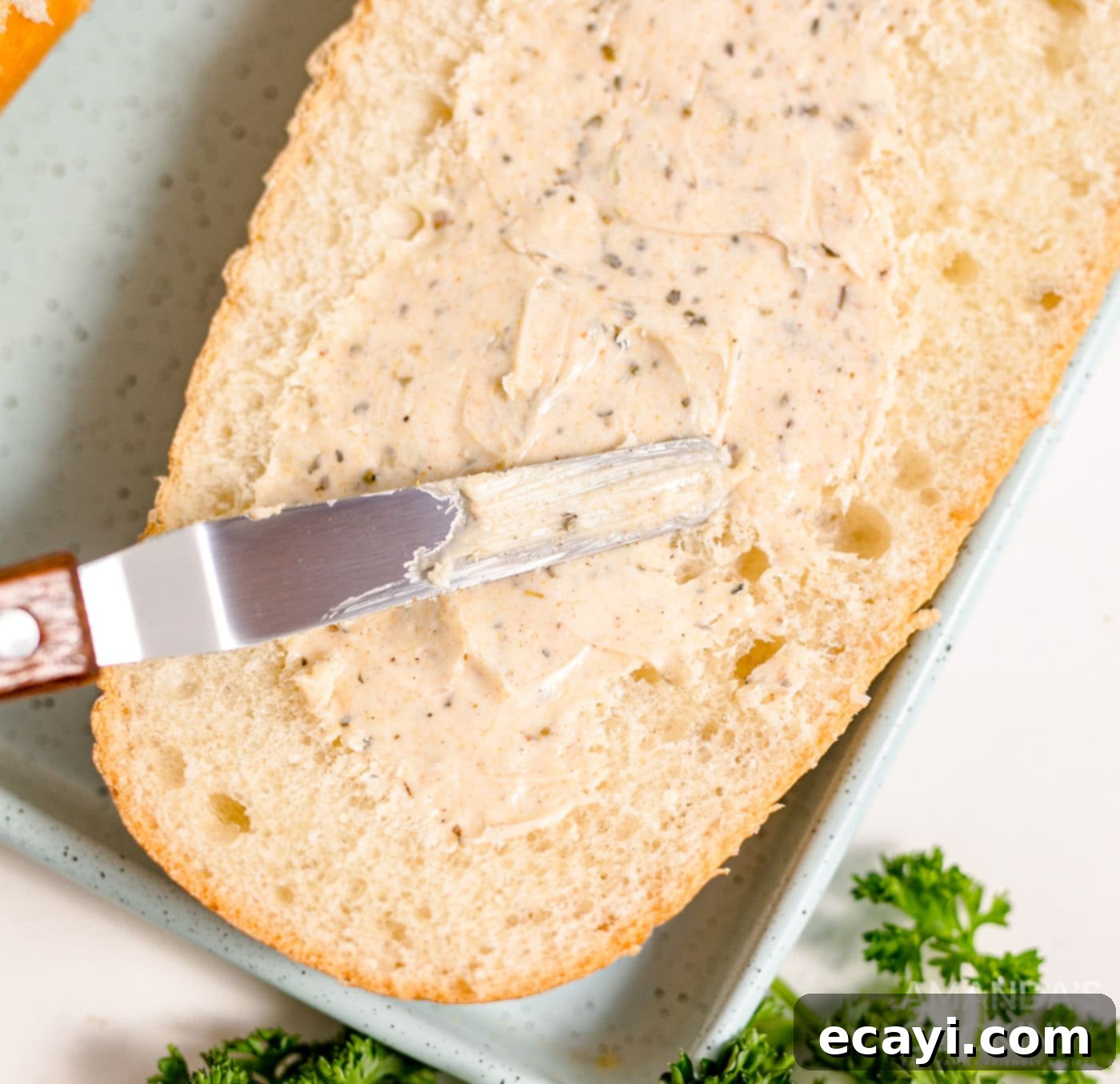 Garlic Cheese Bliss 6 A butter knife spreading seasoned butter mixture onto the cut surface of French bread