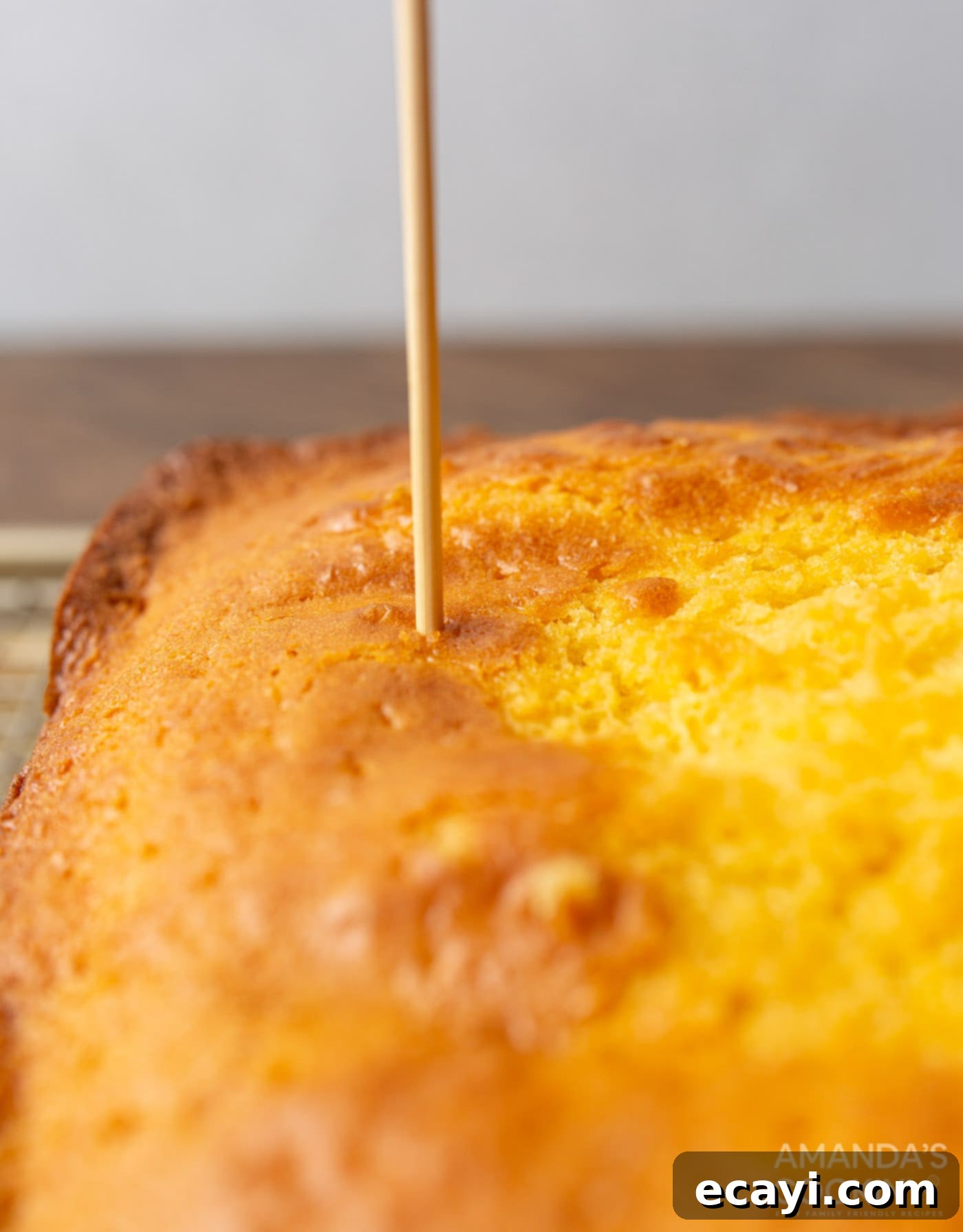 Luscious Pineapple Poke Cake 6 A dowel being used to poke numerous, evenly spaced holes into a freshly baked cake, preparing it for jello infusion.