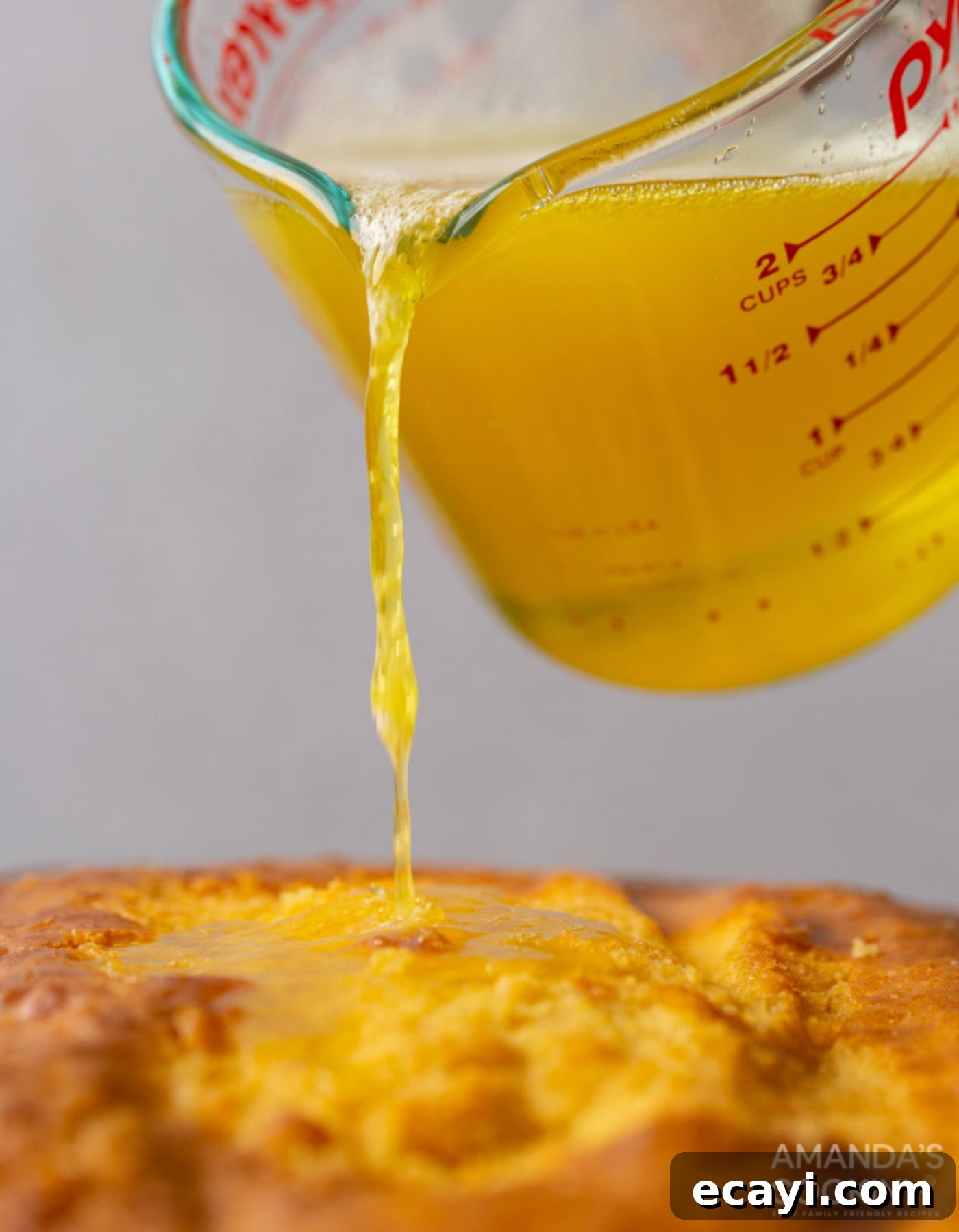 Luscious Pineapple Poke Cake 7 Liquid pineapple jello being slowly poured over the surface of a poked cake, allowing it to soak into the holes.