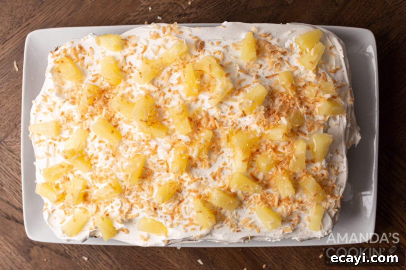 Luscious Pineapple Poke Cake 8 An overhead shot of the finished pineapple poke cake, topped with pineapple chunks, toasted coconut, and ready for serving.