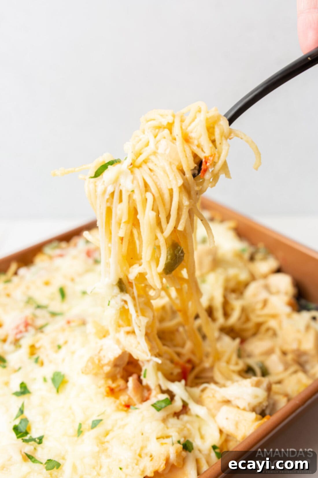 Creamy Chicken Spaghetti Bake 2 Lifting chicken spaghetti with serving fork, showing gooey cheese and tender pasta.
