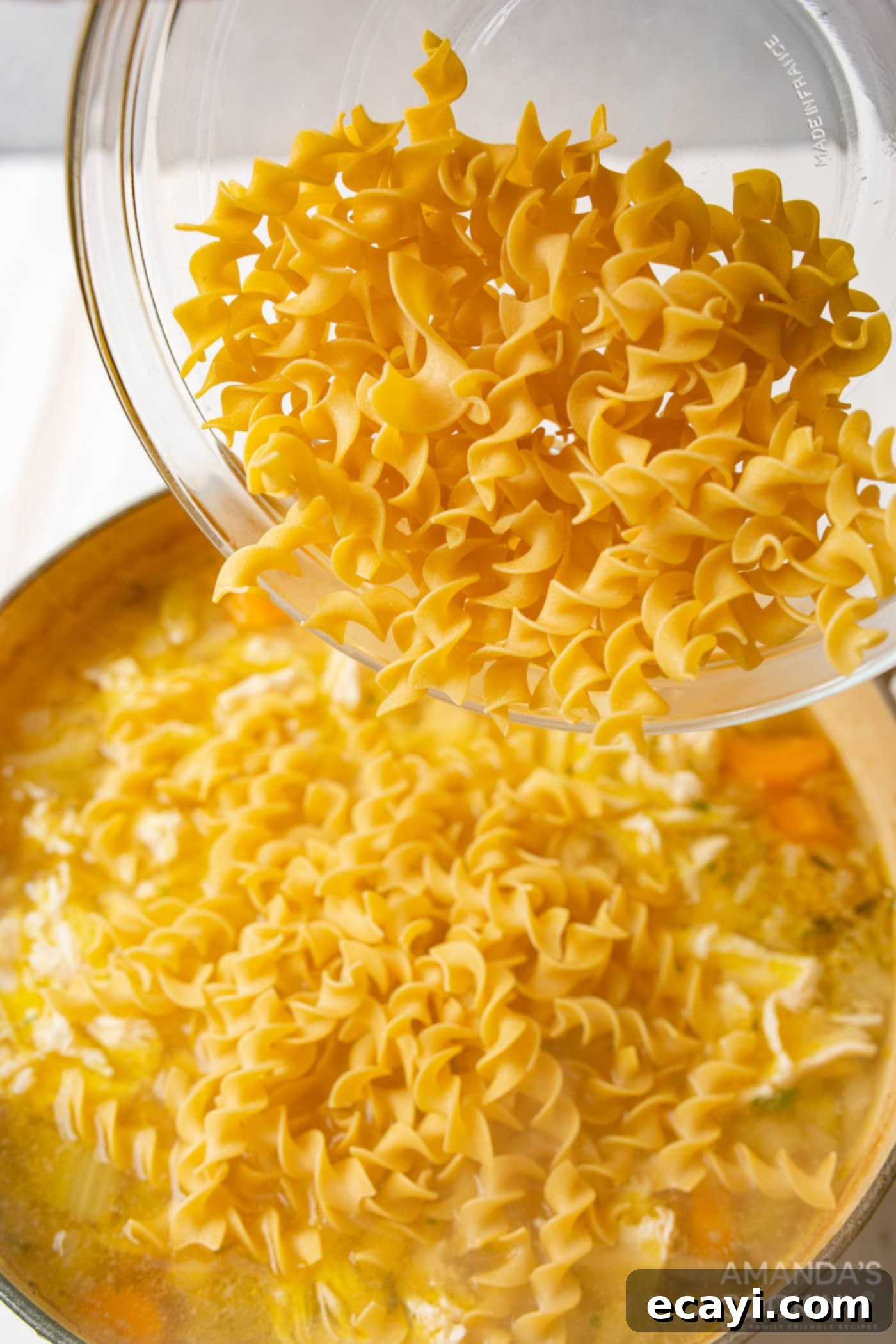 Golden Chicken Noodle Comfort 7 pouring egg noodles into chicken noodle soup broth