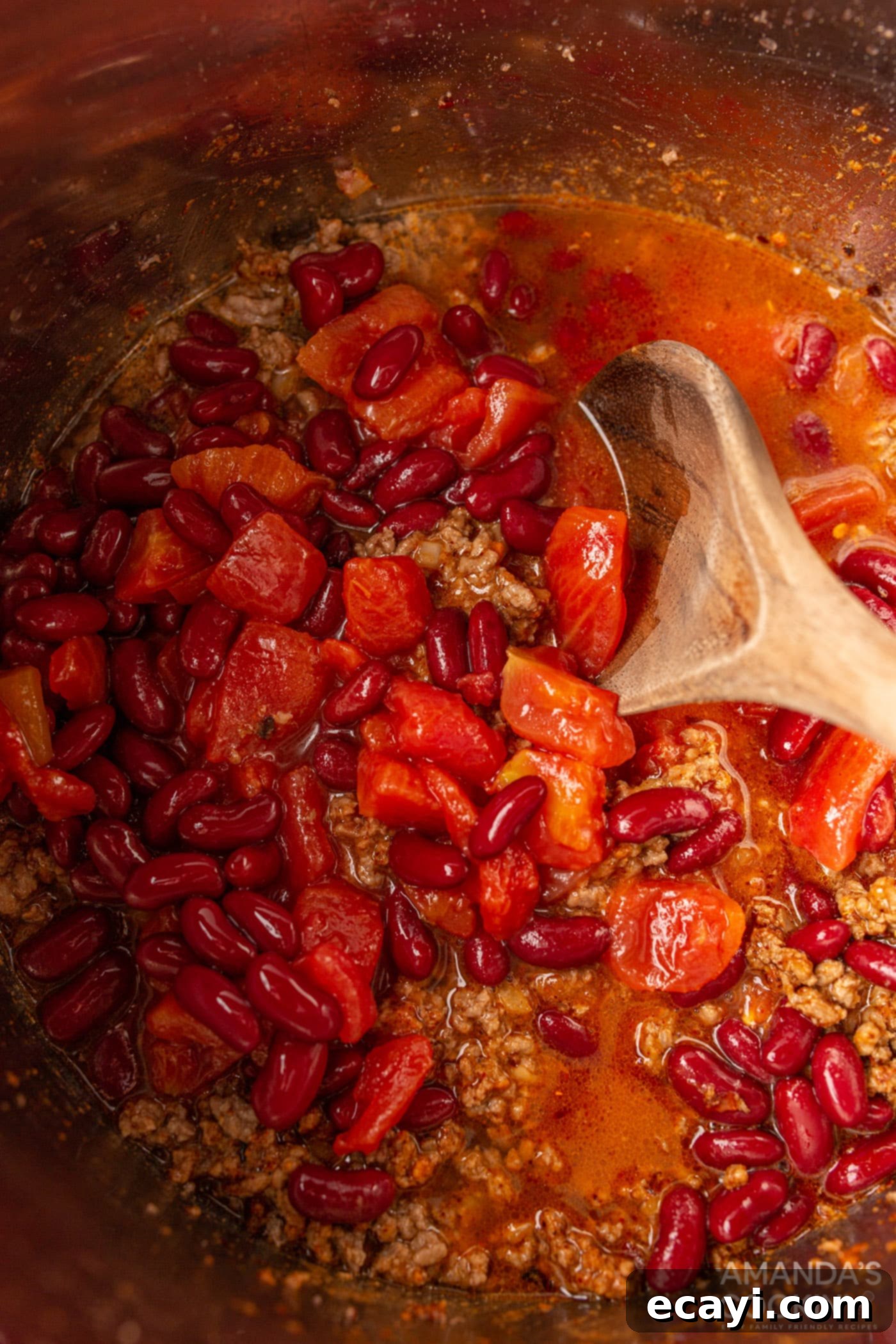 One-Pot Wonder Chili 6 wooden spoon stirring tomatoes into chili