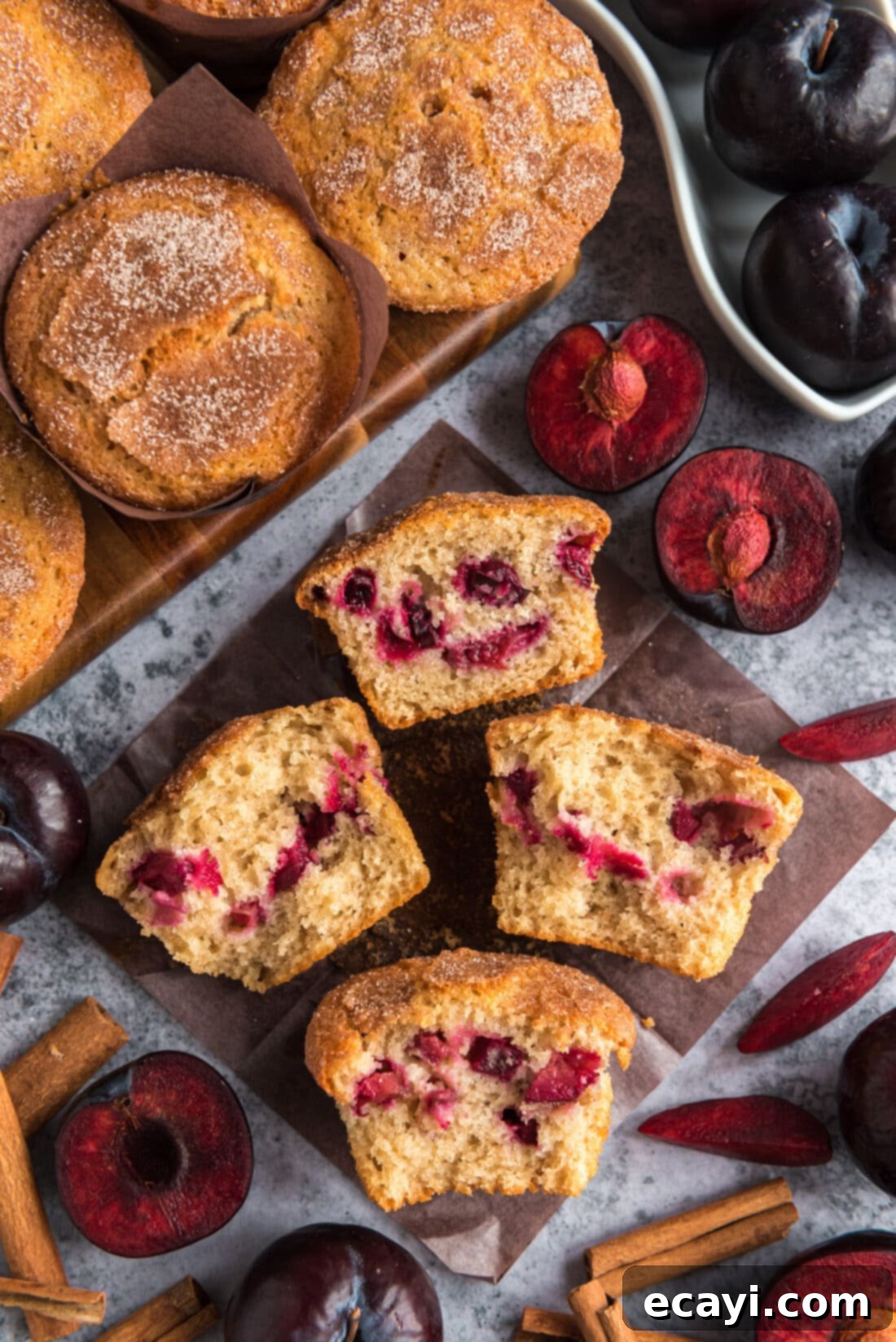 Sparkling Sugar Plum Muffins 2 Two Sugar Crusted Plum Muffins cut in half on parchment paper, showcasing the juicy plum pieces inside and the sugary crust.