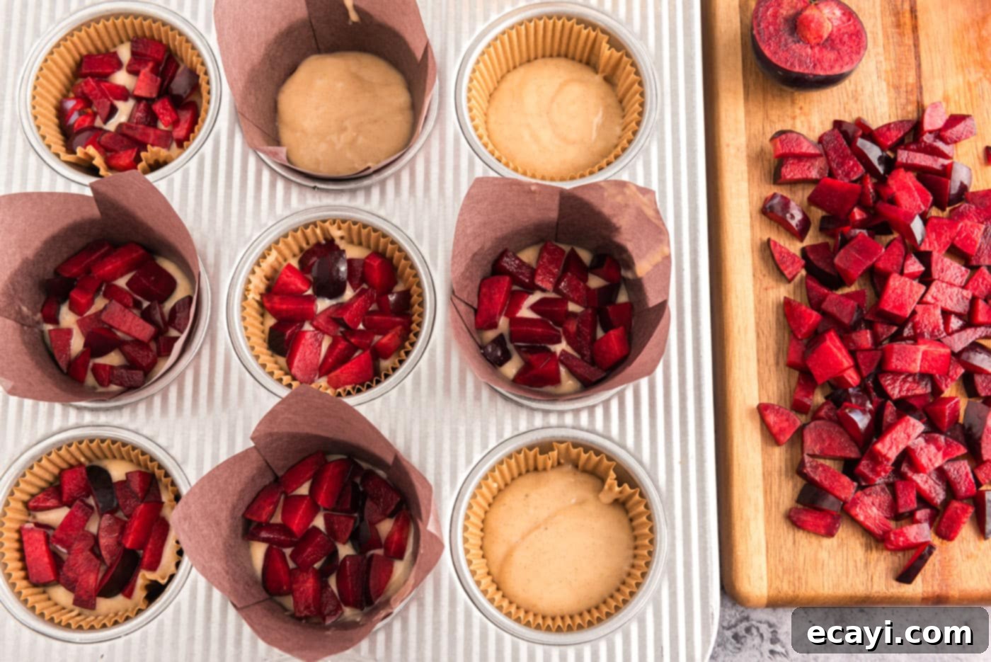Sparkling Sugar Plum Muffins 13 Diced fresh plums being added as a layer on top of muffin batter in a muffin pan.
