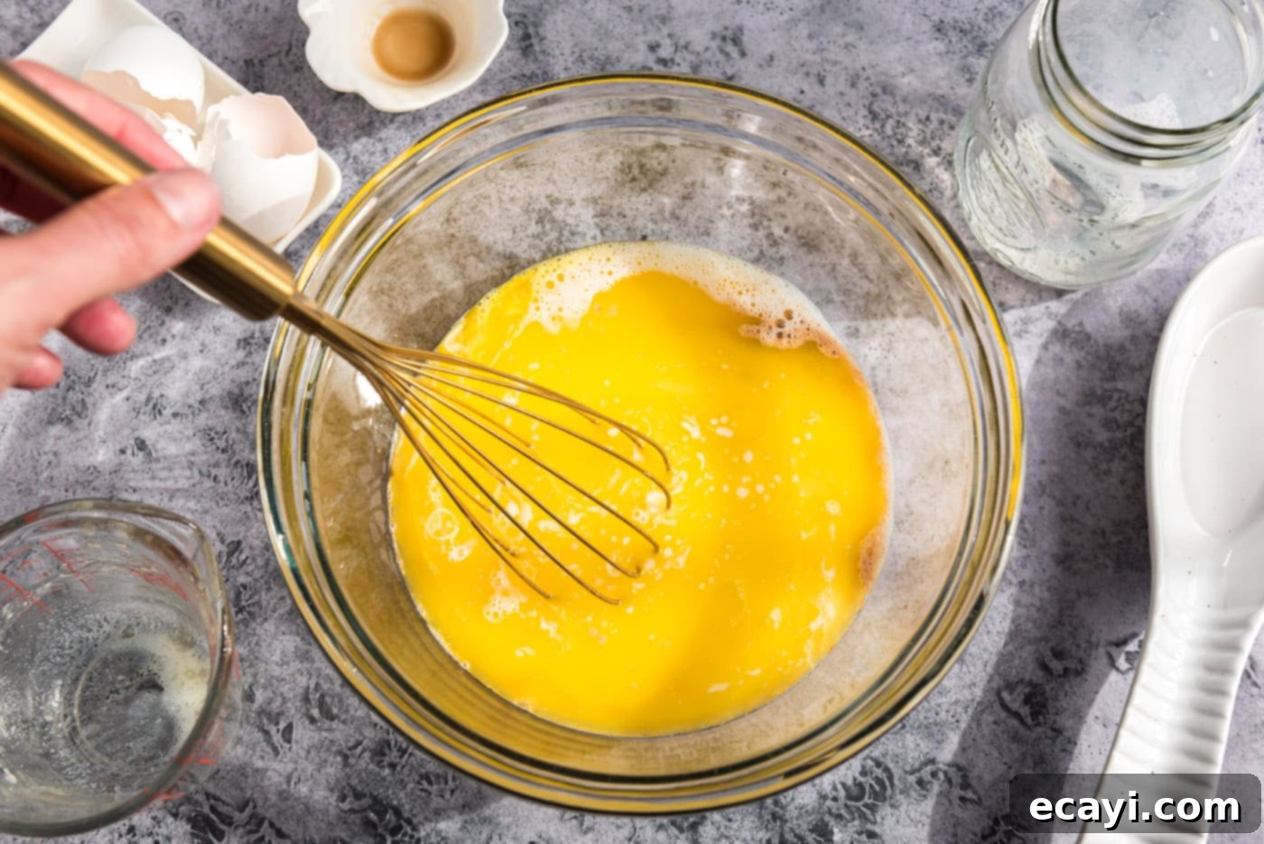 Sparkling Sugar Plum Muffins 7 Close-up of a whisk blending the egg and milk mixture in a bowl, creating a smooth liquid.
