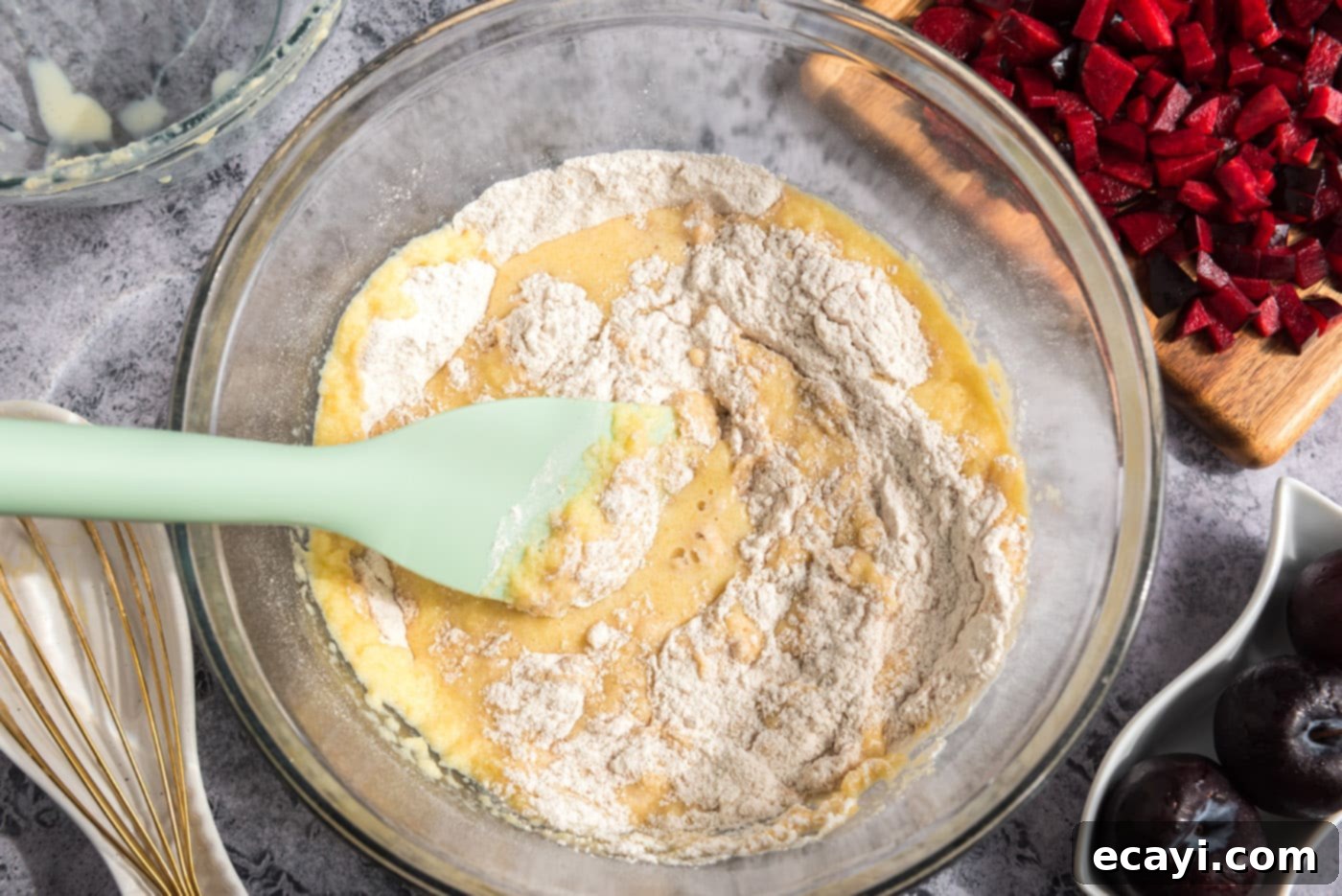 Sparkling Sugar Plum Muffins 10 A rubber spatula gently folding wet and dry ingredients together in a bowl to form muffin batter.