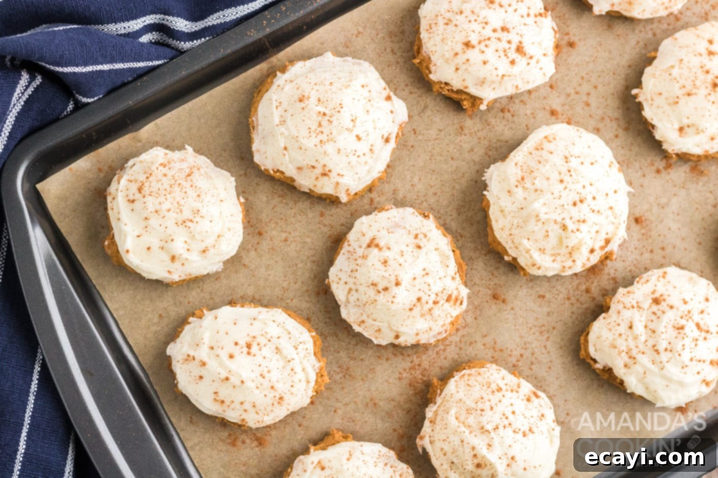 Easy Pumpkin Cake Mix Cookies 9 Cream cheese frosting being spread on pumpkin cake mix cookies on a baking sheet, with cinnamon sprinkled