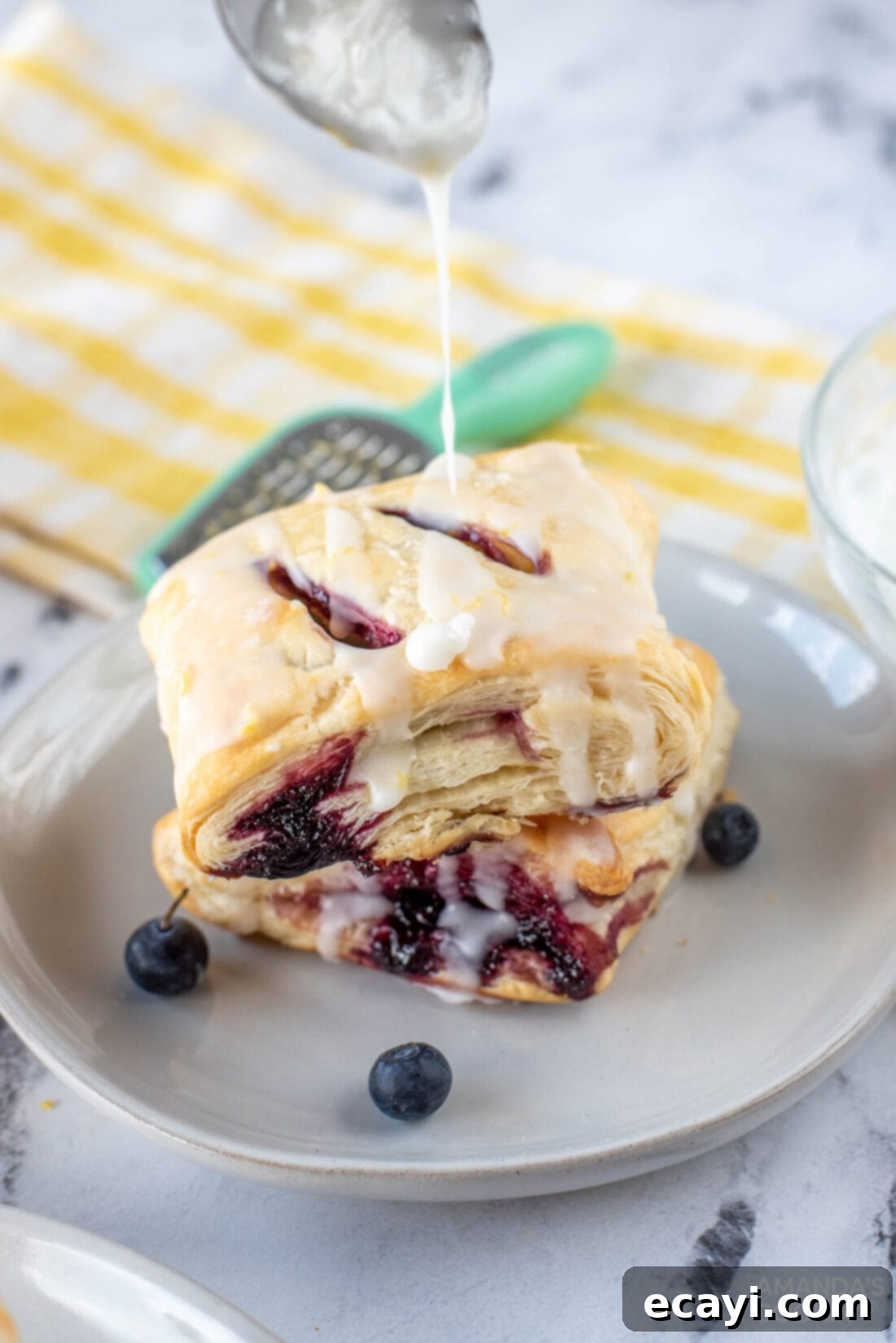 Sunshine Berry Pastry Pockets 13 drizzling glaze onto a stack of Lemon Blueberry Croissant Hand Pies