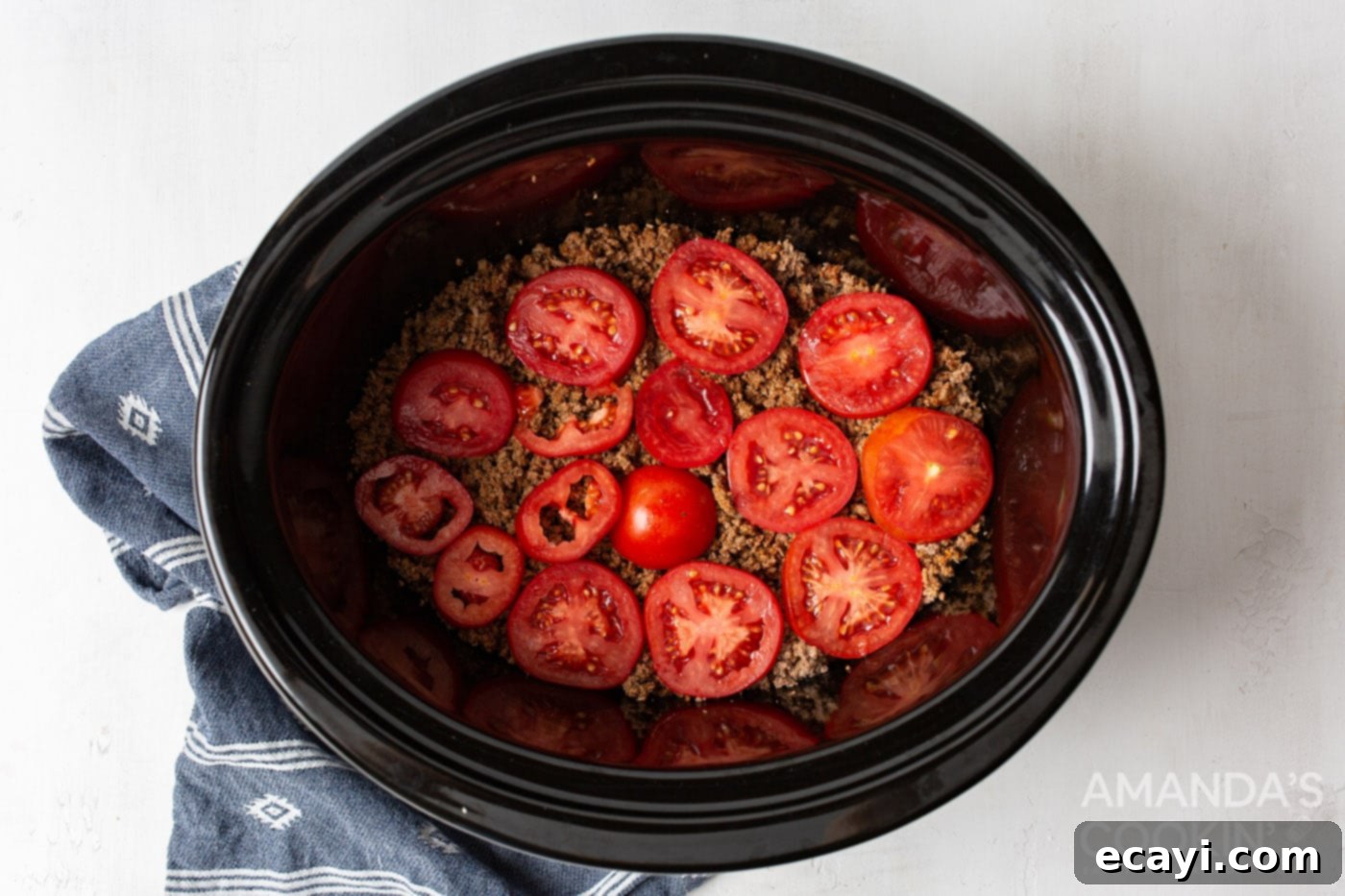 Hearty Slow Cooker John Wayne Casserole 7 tomatoes on top of ground beef in crockpot