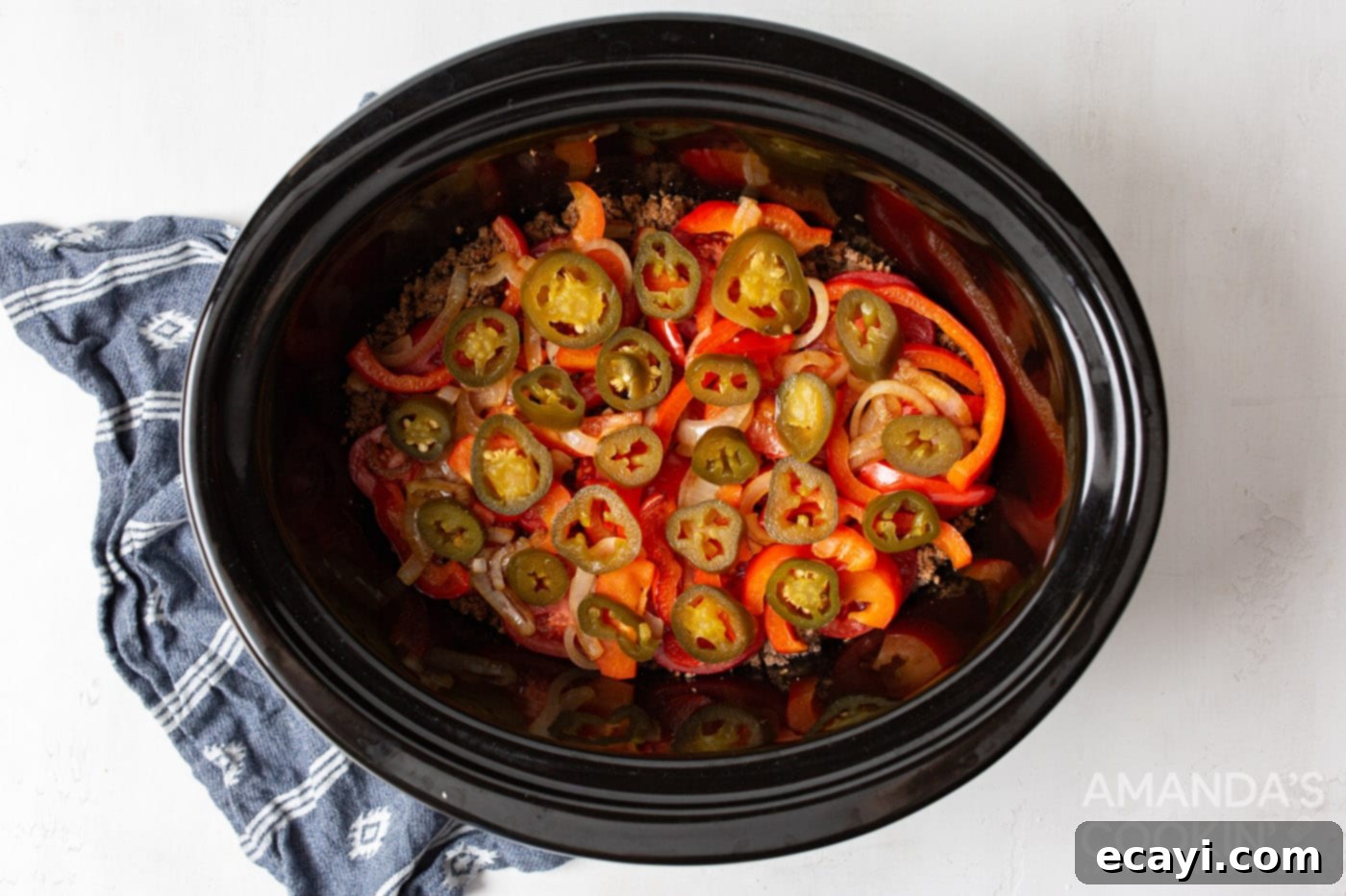 Hearty Slow Cooker John Wayne Casserole 8 jalepenos on top of tomatoes and beef in crockpot