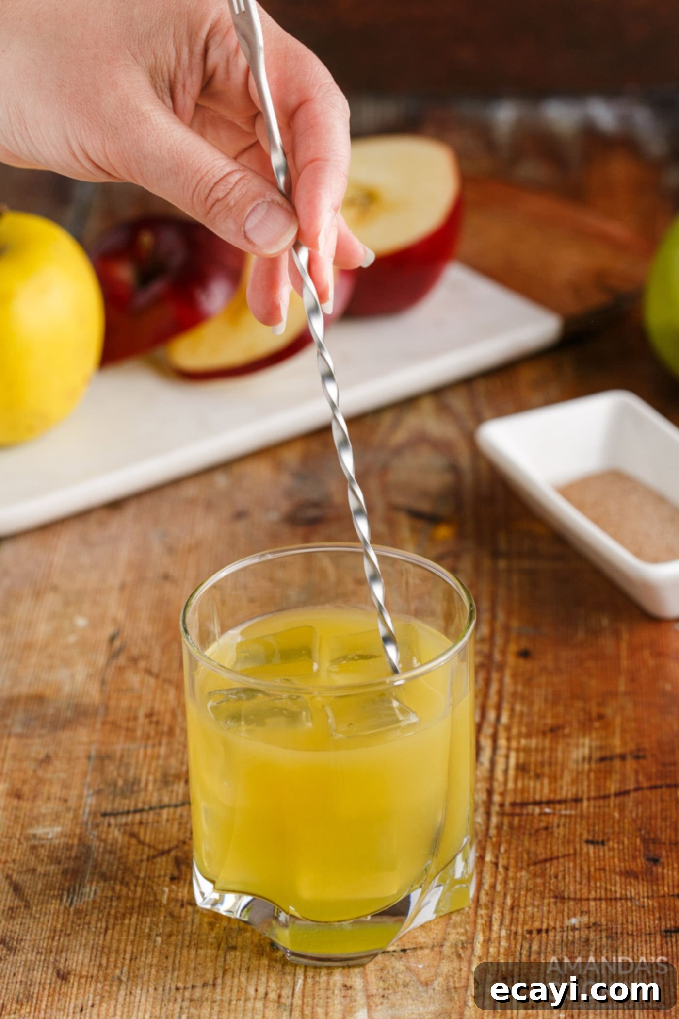 Harvest Spice Apple Elixir 8 hand stirring a Cinnamon Applesauce Cocktail in a rock glass