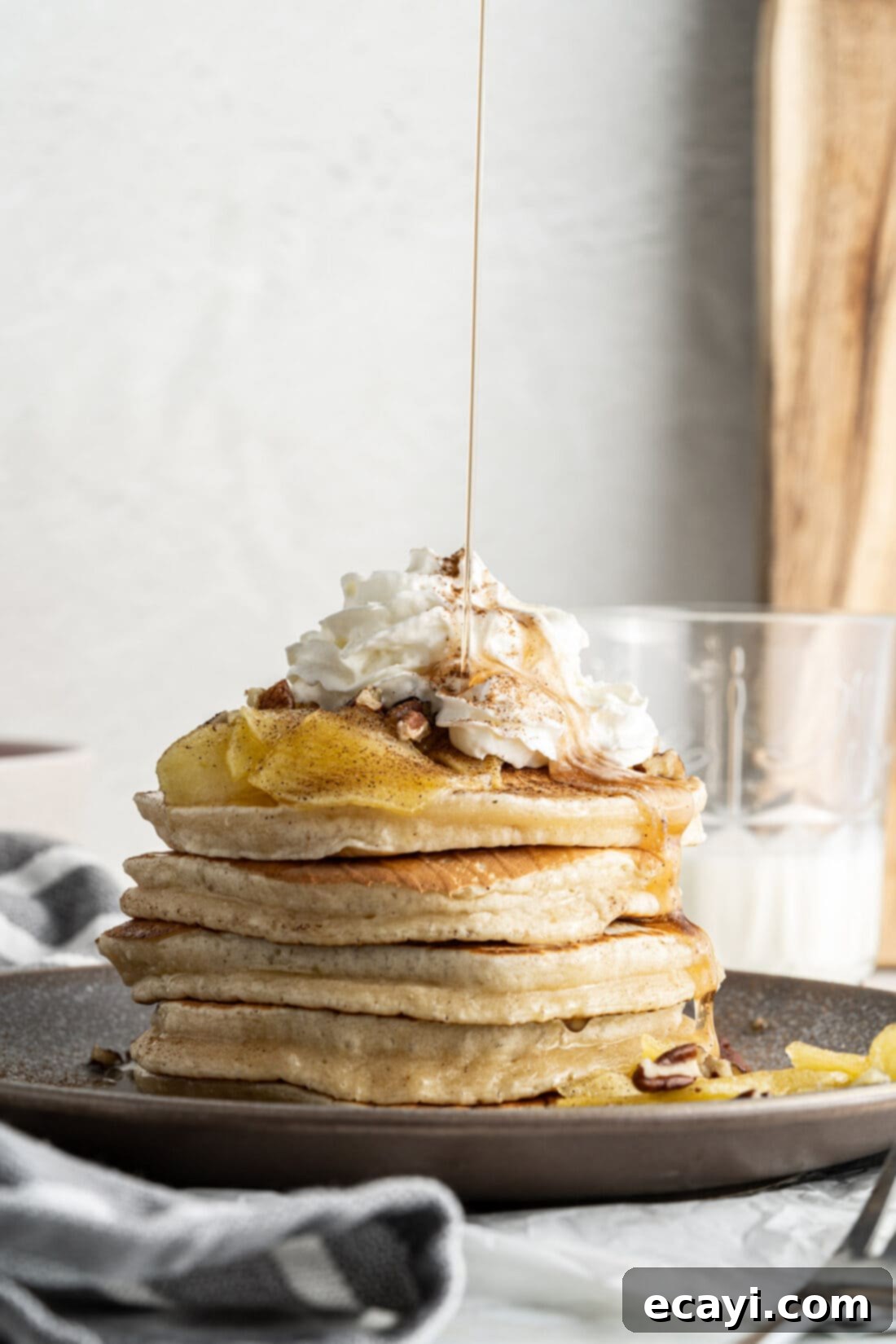 Fluffy Apple Pancakes 2 Drizzling maple syrup onto a stack of fluffy apple pancakes topped with caramelized apples