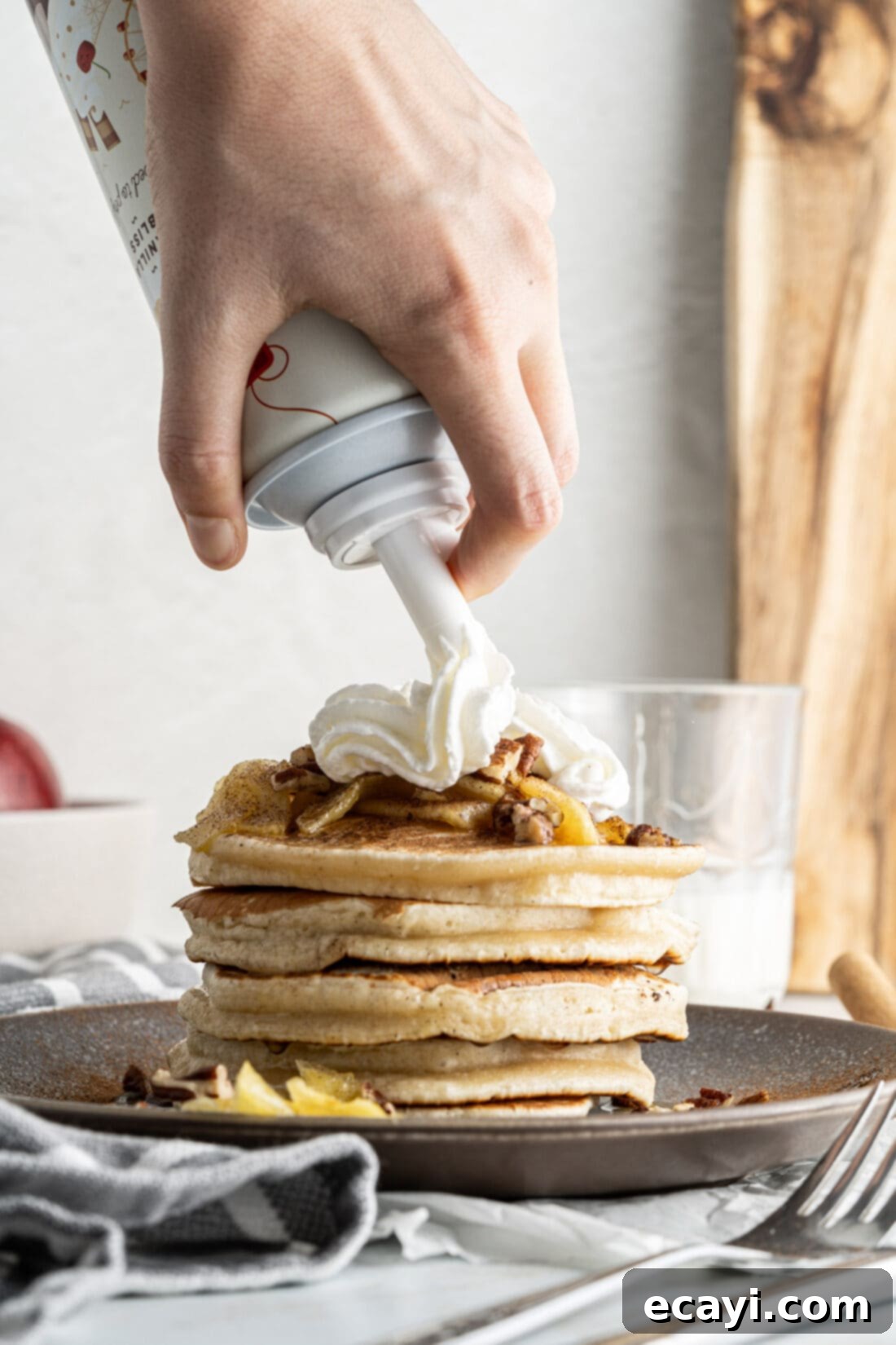 Fluffy Apple Pancakes 11 Adding whipped cream to a stack of apple pancakes, topped with caramelized apples