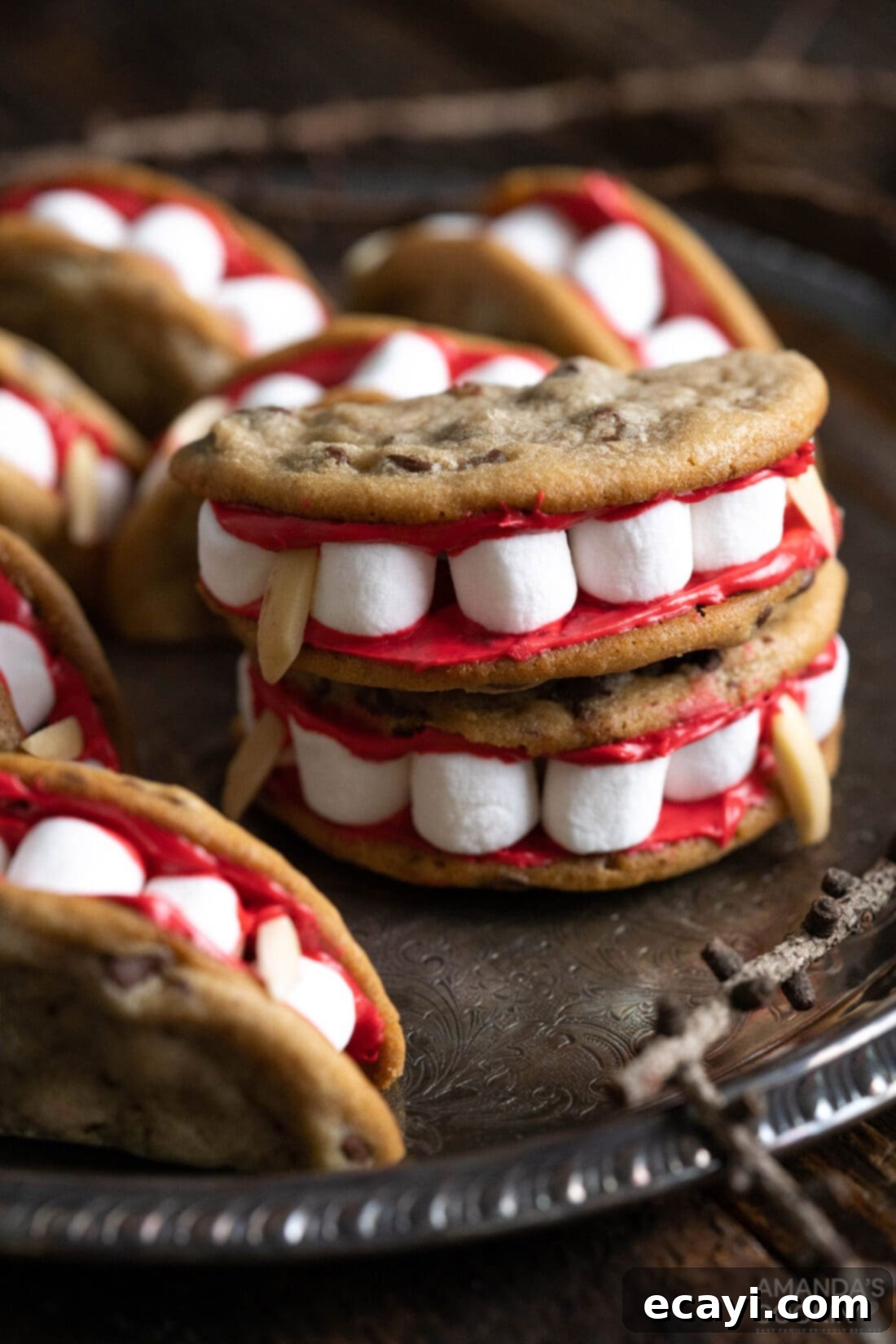 Vampire's Kiss Sandwich Cookies 2 Vampire Sandwich Cookies on a plate, showcasing the red frosting, marshmallow teeth, and almond fangs