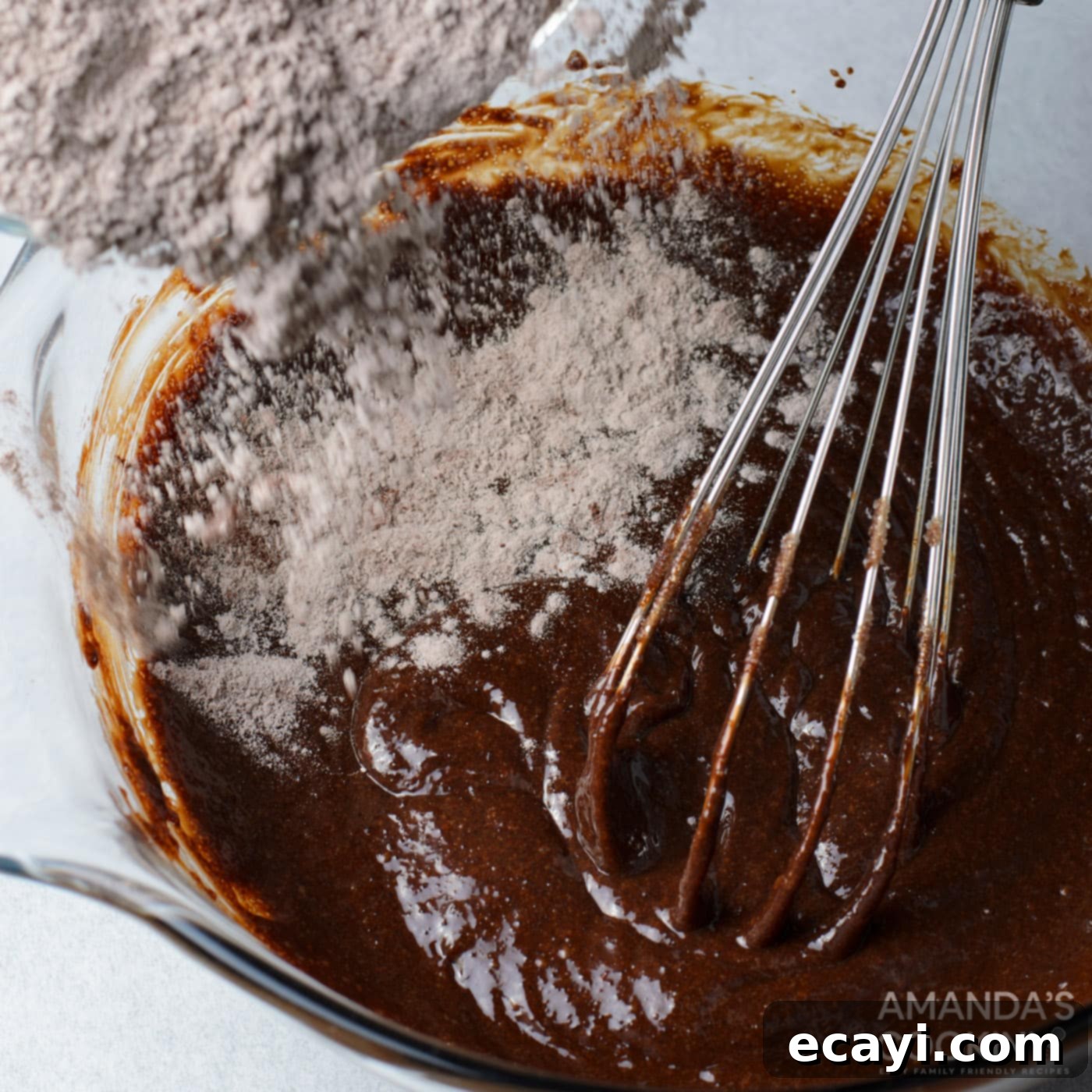 Decadent Oreo Cheesecake Brownies 8 A spatula gently folding dry ingredients into a rich, dark brownie batter in a bowl, ensuring a smooth and perfectly mixed consistency.