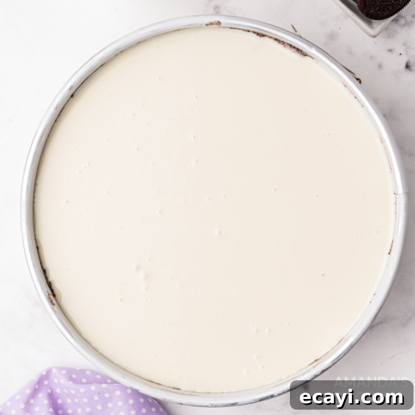 Decadent Oreo Cheesecake 11 Smooth white chocolate ganache spread over the top of the Oreo cheesecake, glistening and ready for chilling.