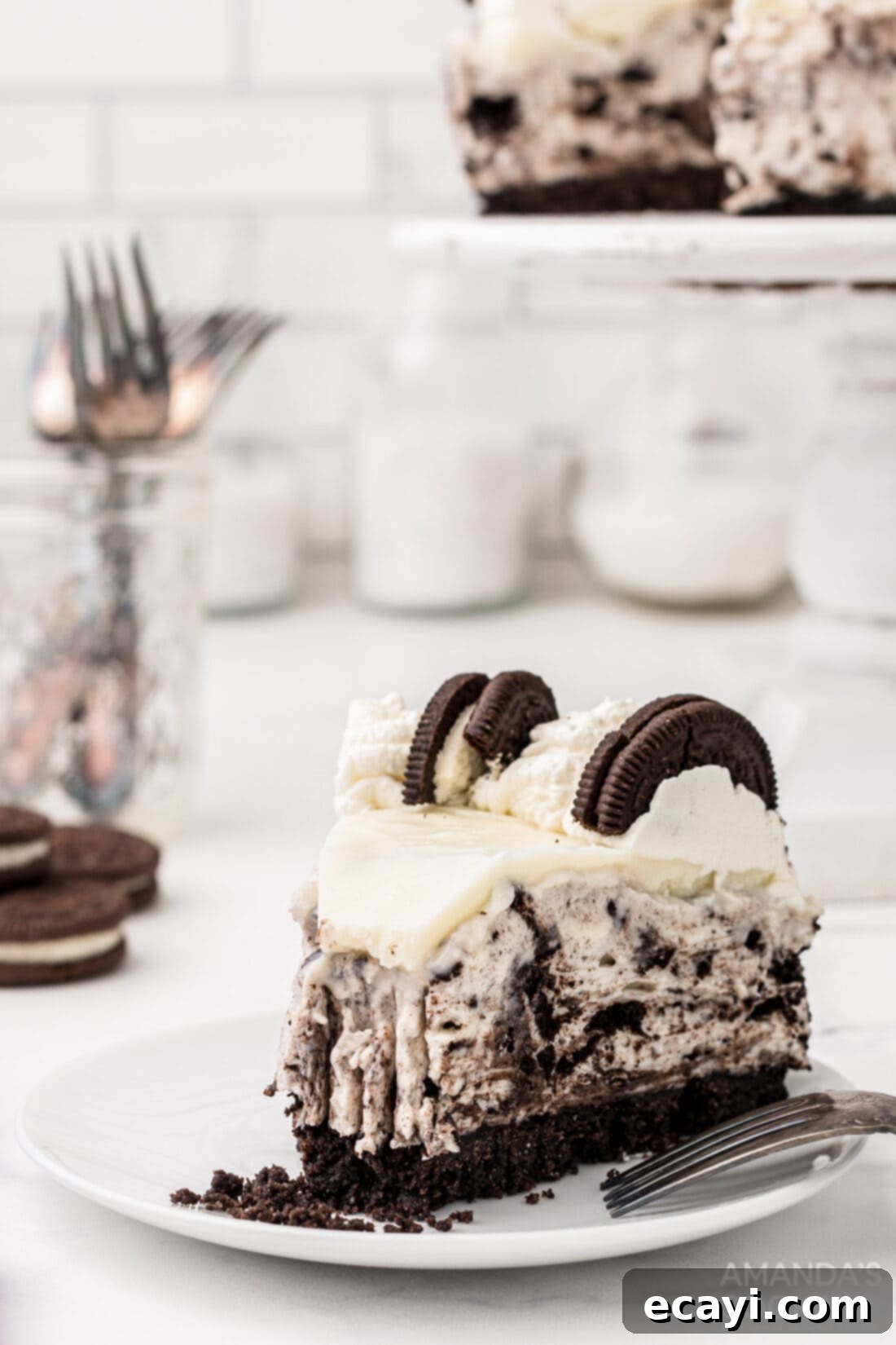 Decadent Oreo Cheesecake 3 A perfectly cut slice of rich Oreo Cheesecake, showing the dense cookie crust, the creamy filling with visible Oreo chunks, and the elegant white ganache topping with whipped cream.