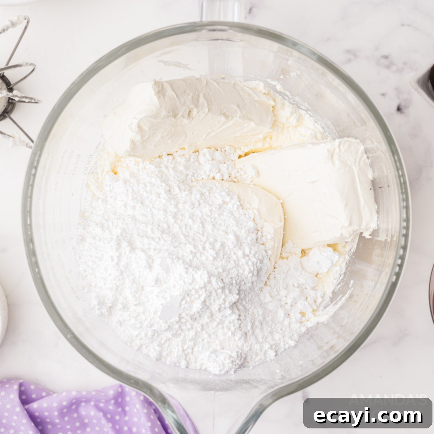 Decadent Oreo Cheesecake 7 Cream cheese and powdered sugar being mixed together in a large bowl, creating a smooth and creamy cheesecake batter.