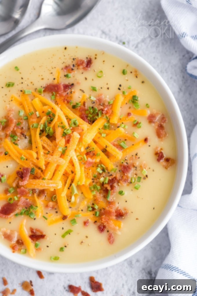 Pure comfort food, this creamy potato cheese soup is topped with crumbled bacon and chives. Made with extra sharp cheddar cheese for the best flavor.  Close-up overhead shot of a steaming bowl of creamy cheddar potato soup, garnished with crispy bacon and fresh chives
