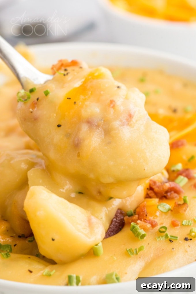 Pure comfort food, this creamy potato cheese soup is topped with crumbled bacon and chives. Made with extra sharp cheddar cheese for the best flavor.  A spoonful of chunky, creamy potato and cheese soup being lifted from a bowl, showcasing its rich texture
