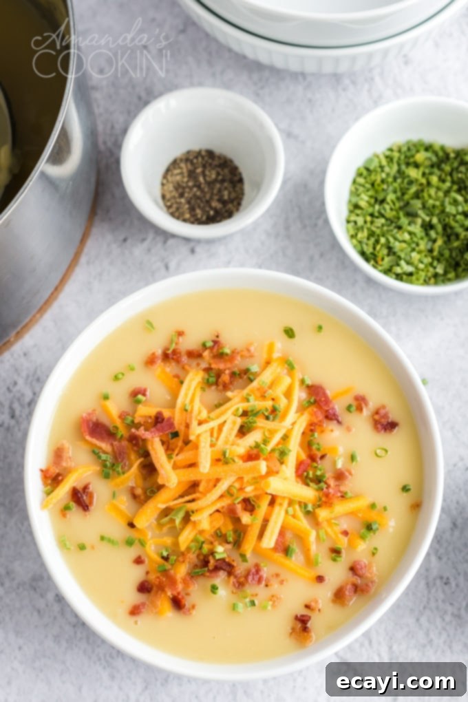 Pure comfort food, this creamy potato cheese soup is topped with crumbled bacon and chives. Made with extra sharp cheddar cheese for the best flavor.  A beautifully presented bowl of creamy potato cheese soup, garnished with green chives, with a smaller bowl of fresh chives in the soft background