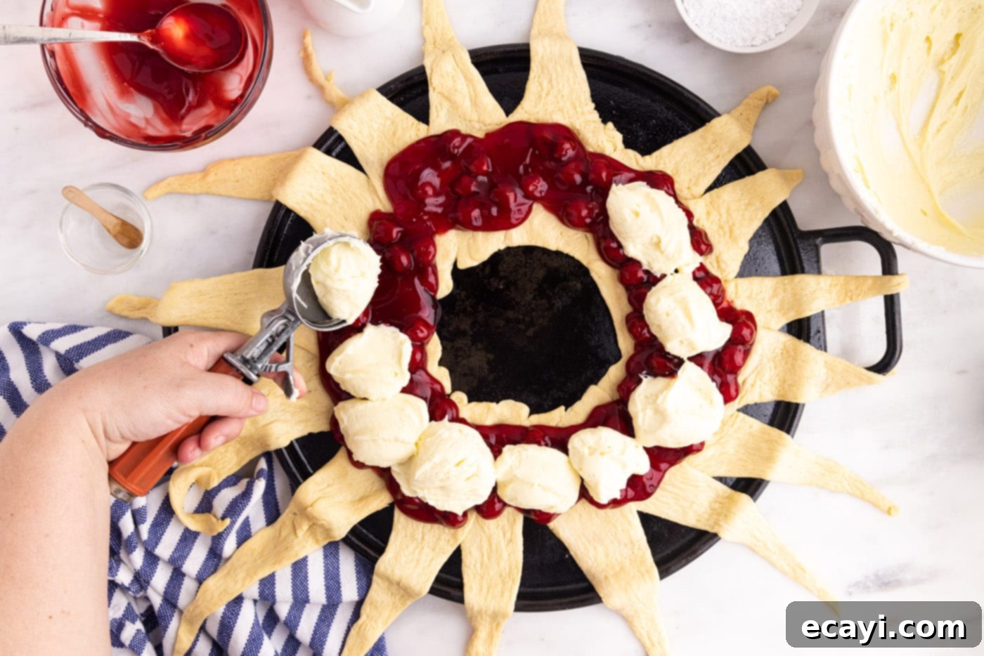 Artisan Danish Wreath 7 Cream cheese mixture being added on top of the cherry pie filling on the crescent roll base.