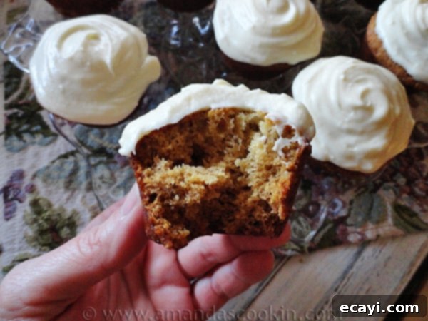 Half-Eaten Banana Cupcake with Cream Cheese Frosting A close-up photo of a half-eaten banana cupcake, revealing its moist interior, with other fully frosted cupcakes blurred in the background, all topped with creamy vanilla cream cheese frosting.