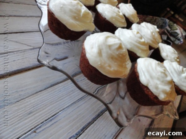 Banana Cupcakes with Cream Cheese Frosting on a Cake Stand A collection of beautifully arranged banana cupcakes, each generously swirled with vanilla cream cheese frosting, resting on an elegant clear cake stand.