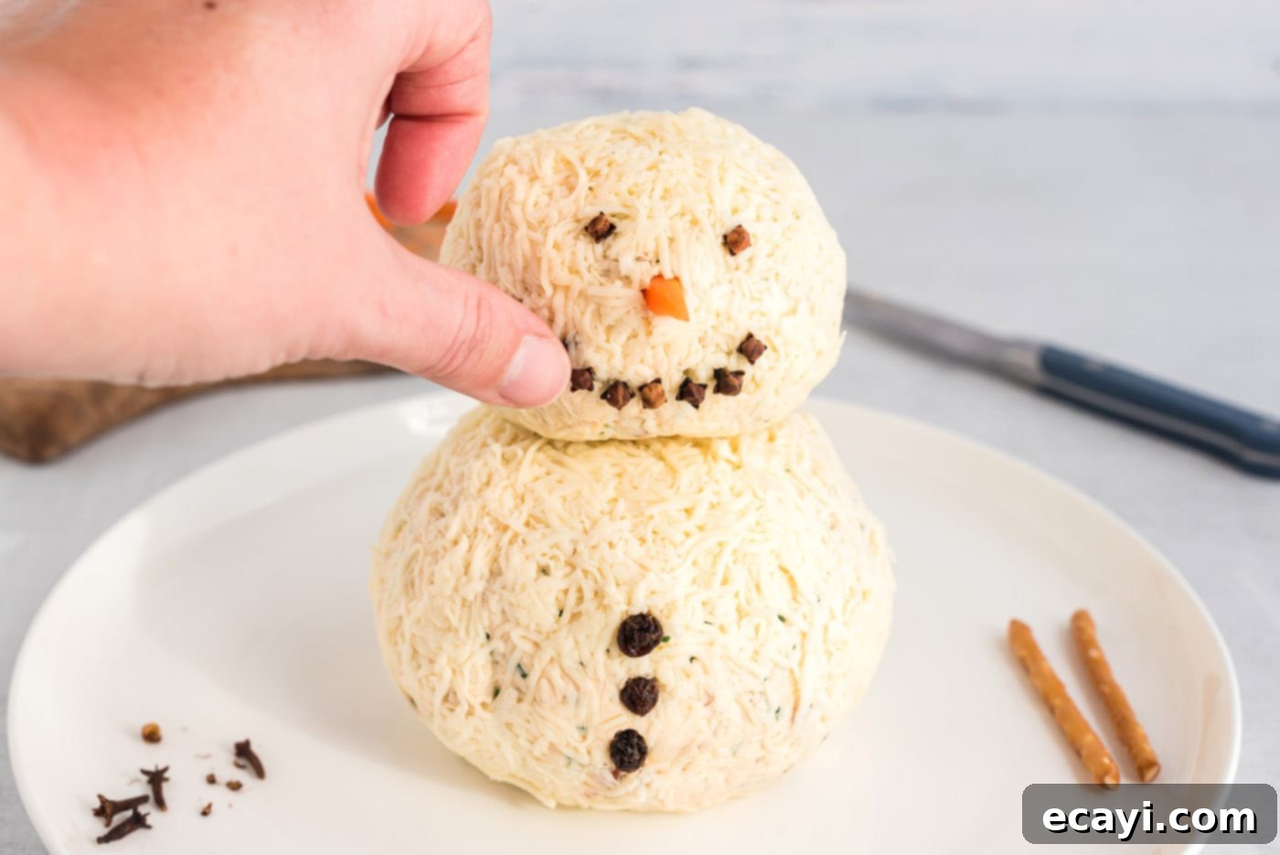 Jolly Snowman Cheeseball 11 hand pressing cloves into snowman cheeseball