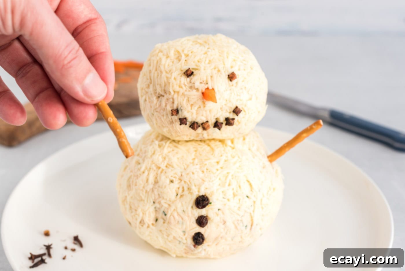 Jolly Snowman Cheeseball 12 hand adding a pretzel stick to snowman cheeseball
