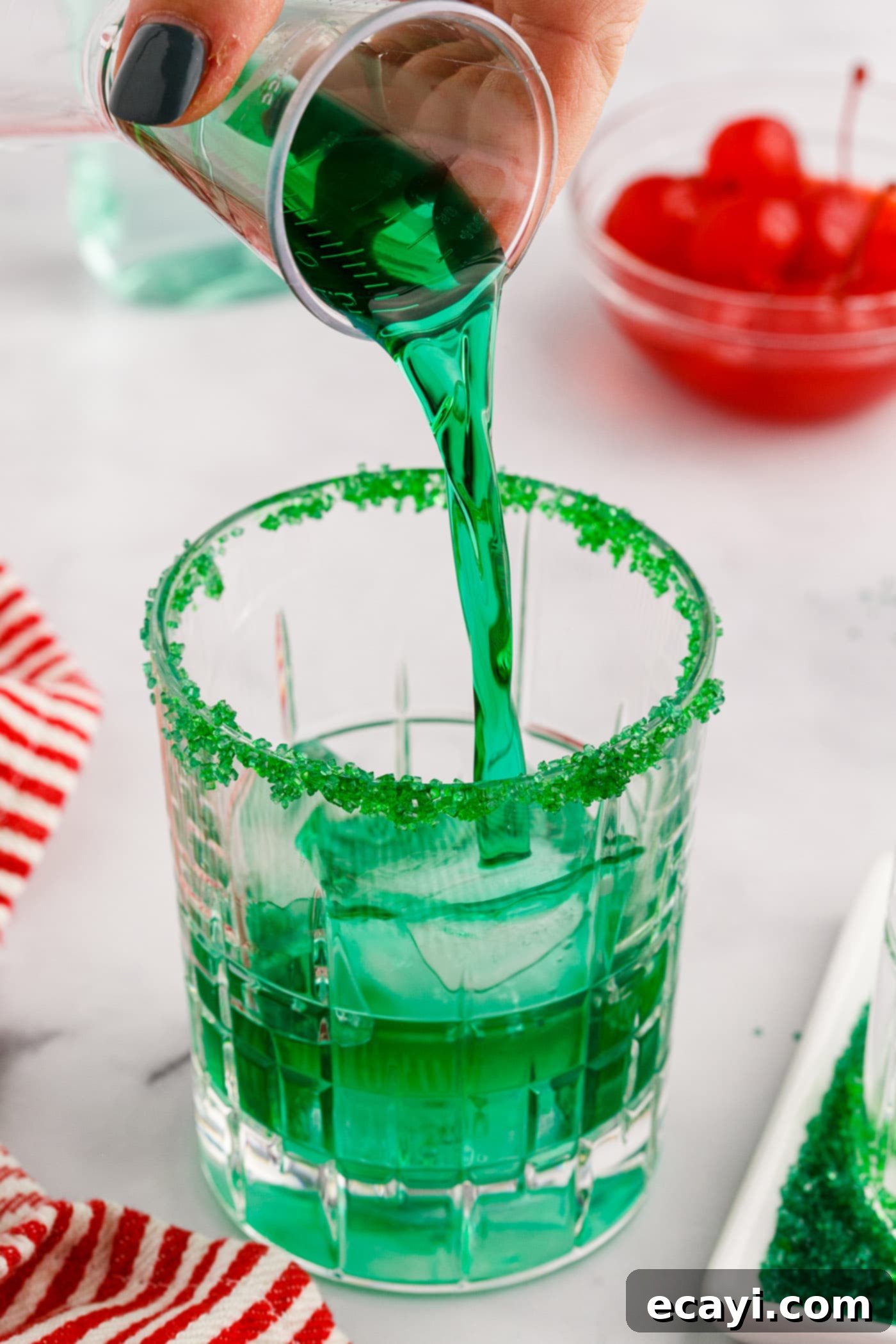 Grinch's Emerald Elixir 5 Pouring bright green Midori into a rock glass filled with ice, preparing a Grinch Cocktail.