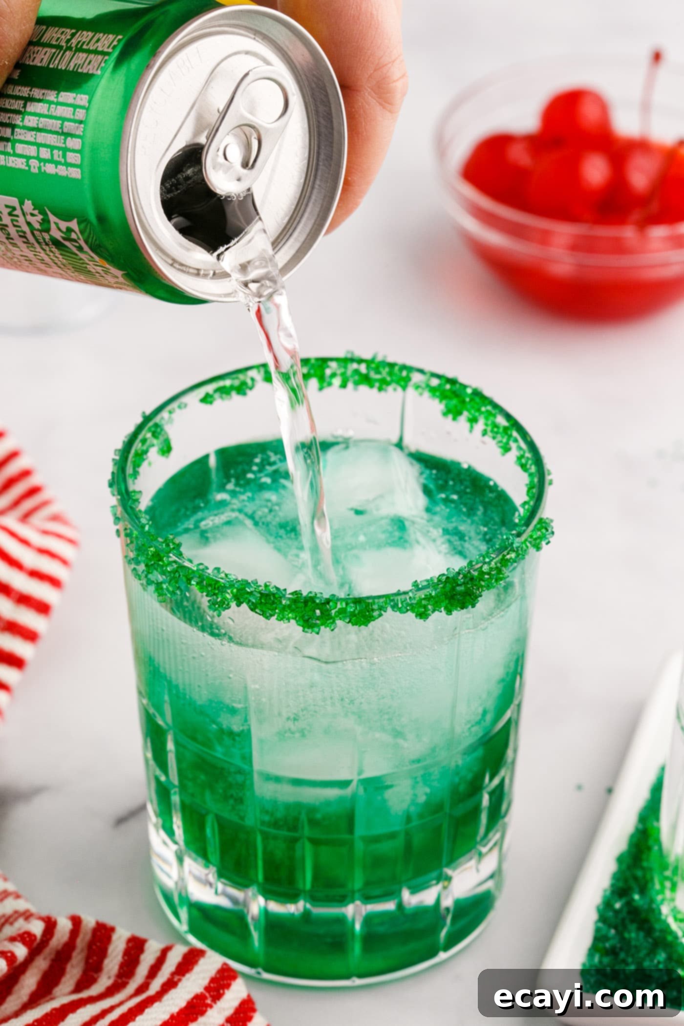Grinch's Emerald Elixir 6 Topping a Grinch cocktail with lemon-lime soda in a glass with a green sugared rim.