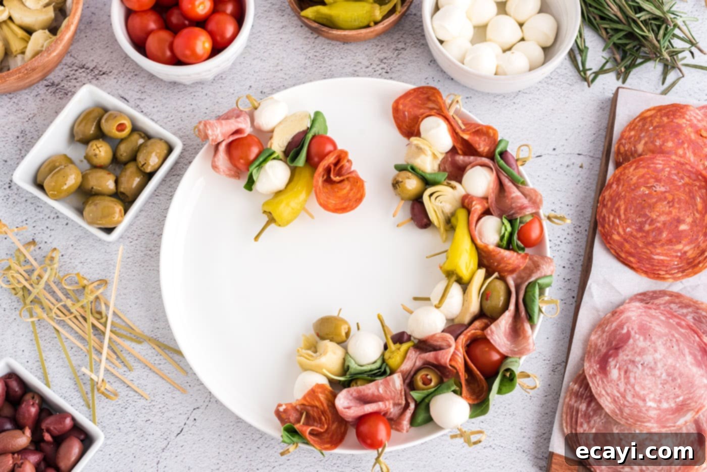 Gourmet Grazing Wreath 7 Artfully arranged antipasto skewers on a plate, forming the base of the wreath before adding rosemary.
