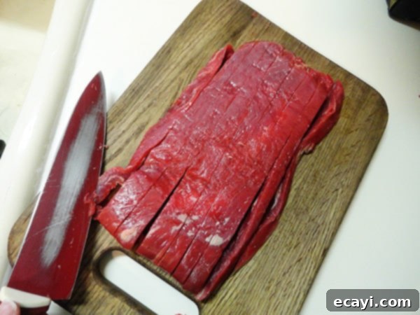 Expertly Diced Flank Steak for Tacos An overhead photo of thinly diced flank steak on a wooden cutting board, ready for seasoning and cooking.