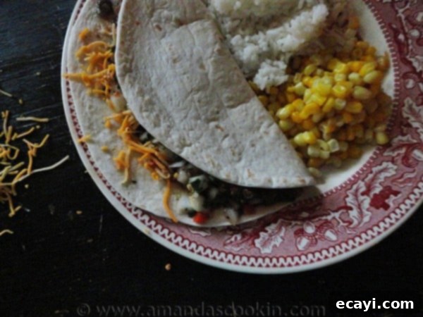 Flank Steak Soft Tacos Ready to Serve An overhead photo of a delicious flank steak soft taco resting on a plate with corn and rice to the side, garnished with cilantro.