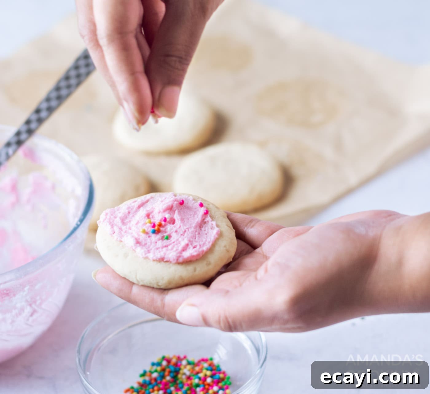Soft Frosted Lofthouse Cookies 8 A hand adding colorful sprinkles to a frosted Lofthouse cookie.