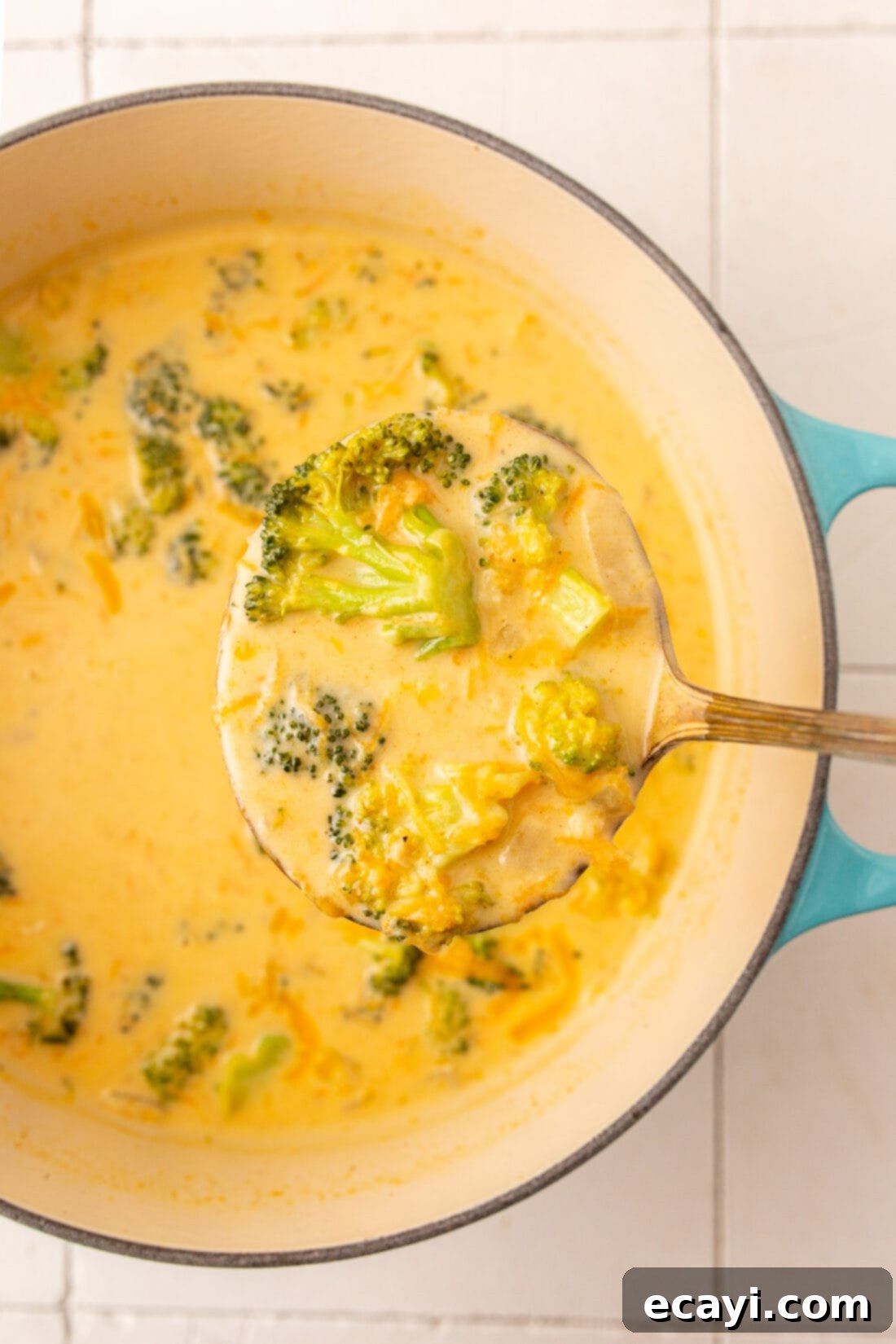Golden Broccoli Cheddar Delight 2 A ladle serving a generous portion of creamy homemade broccoli cheese soup into a bowl.