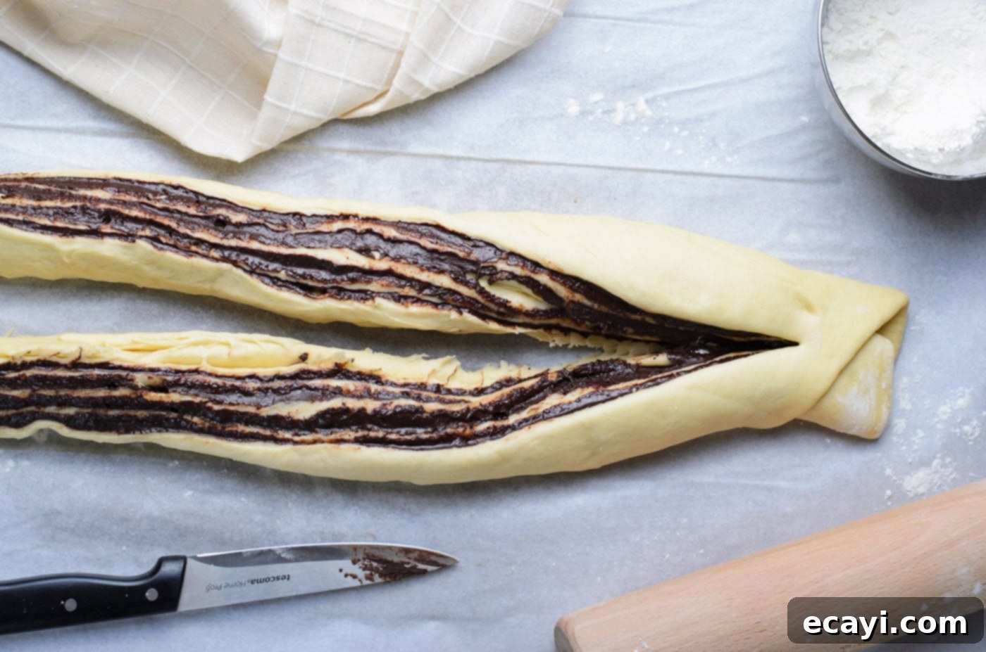 Swirling Chocolate Delight 13 Chocolate babka dough log expertly sliced in half lengthwise, with one end remaining connected, beautifully exposing the chocolate swirls.