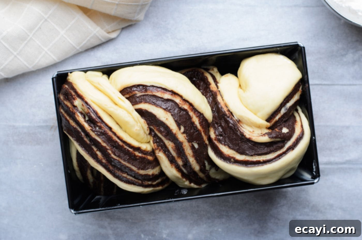 Swirling Chocolate Delight 15 Braided chocolate babka dough gently placed in a loaf pan and covered loosely with plastic, undergoing its crucial second rise.