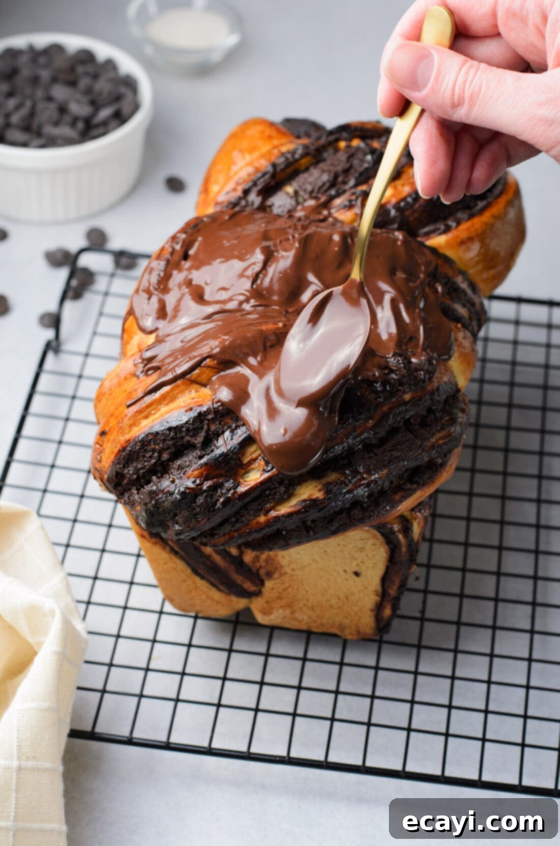 Swirling Chocolate Delight 16 A skilled hand generously spooning rich, glossy chocolate glaze over a freshly baked and cooled chocolate babka loaf on a wire rack.