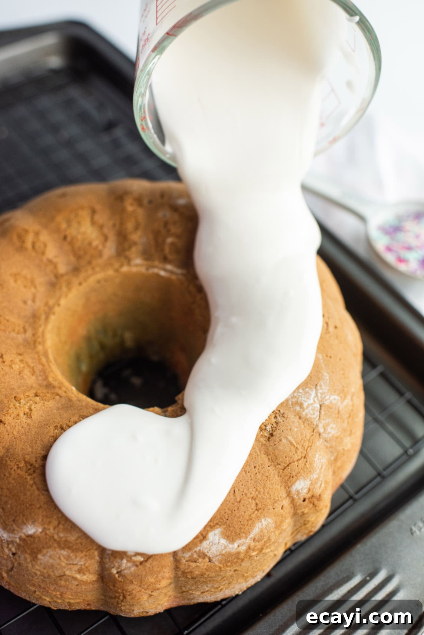 Enchanted Rainbow Bundt 11 Pouring vanilla glaze over the cooled Unicorn Bundt Cake on a wire rack.