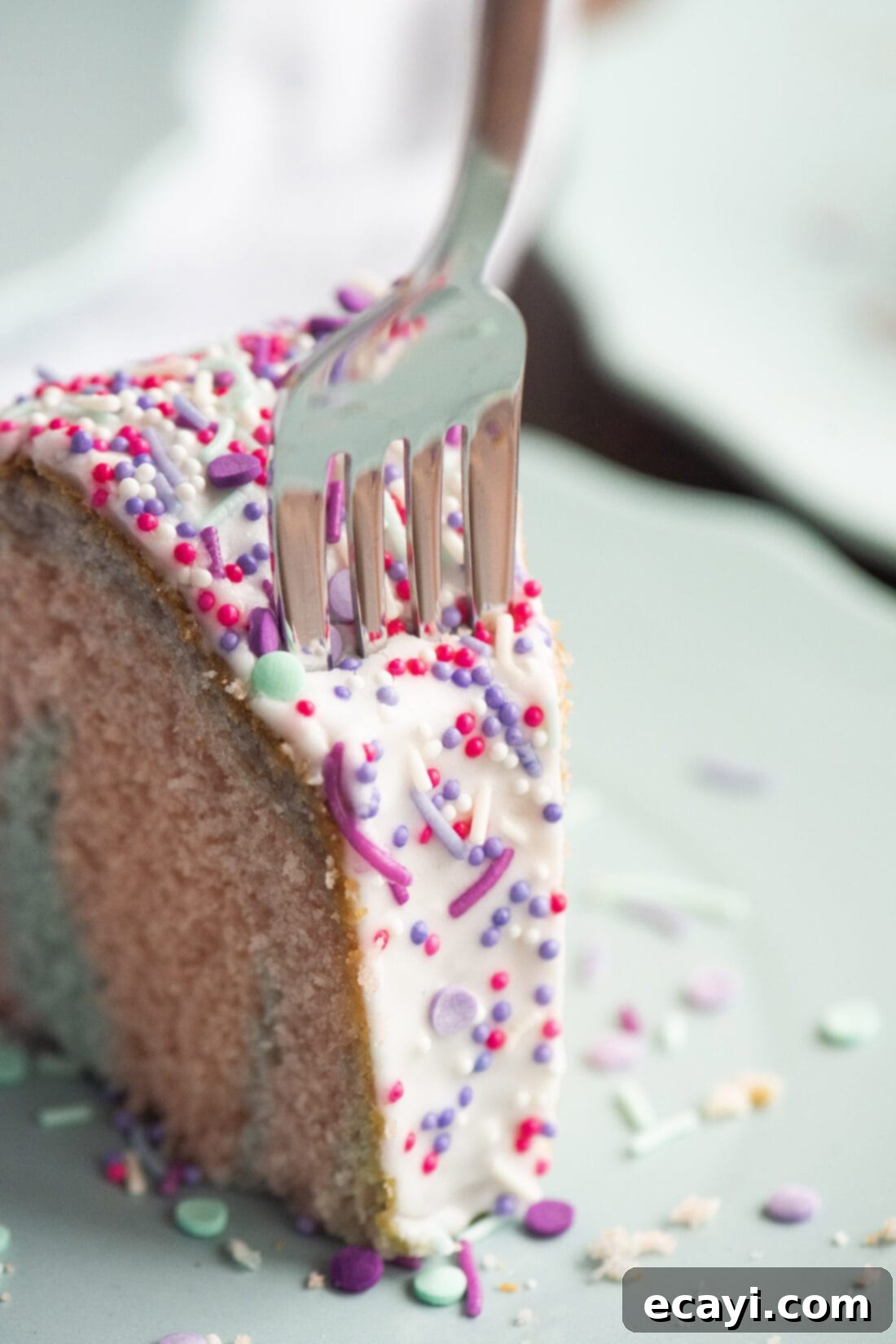 Enchanted Rainbow Bundt 3 Close-up of a slice of Unicorn Bundt Cake with a fork, showing the vibrant pastel layers.