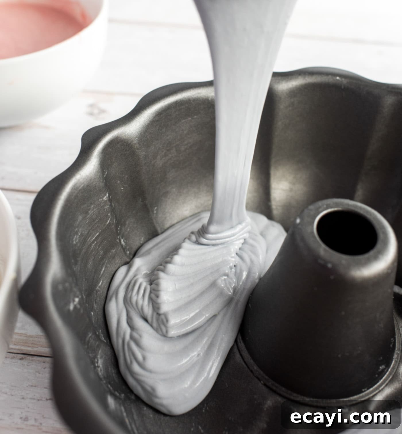 Enchanted Rainbow Bundt 8 Pouring pastel purple cake batter into a bundt pan.
