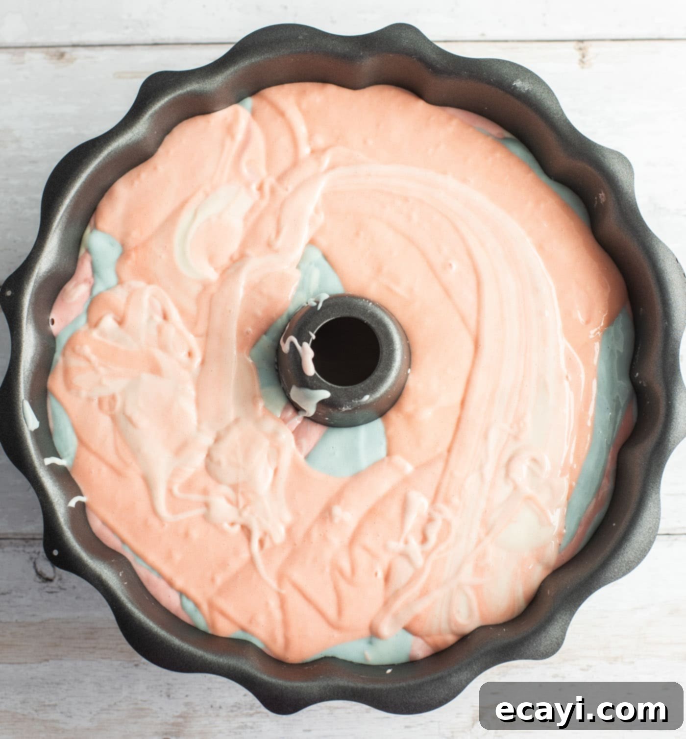 Enchanted Rainbow Bundt 10 Bundt pan filled with layers of pastel colored cake batter before baking.