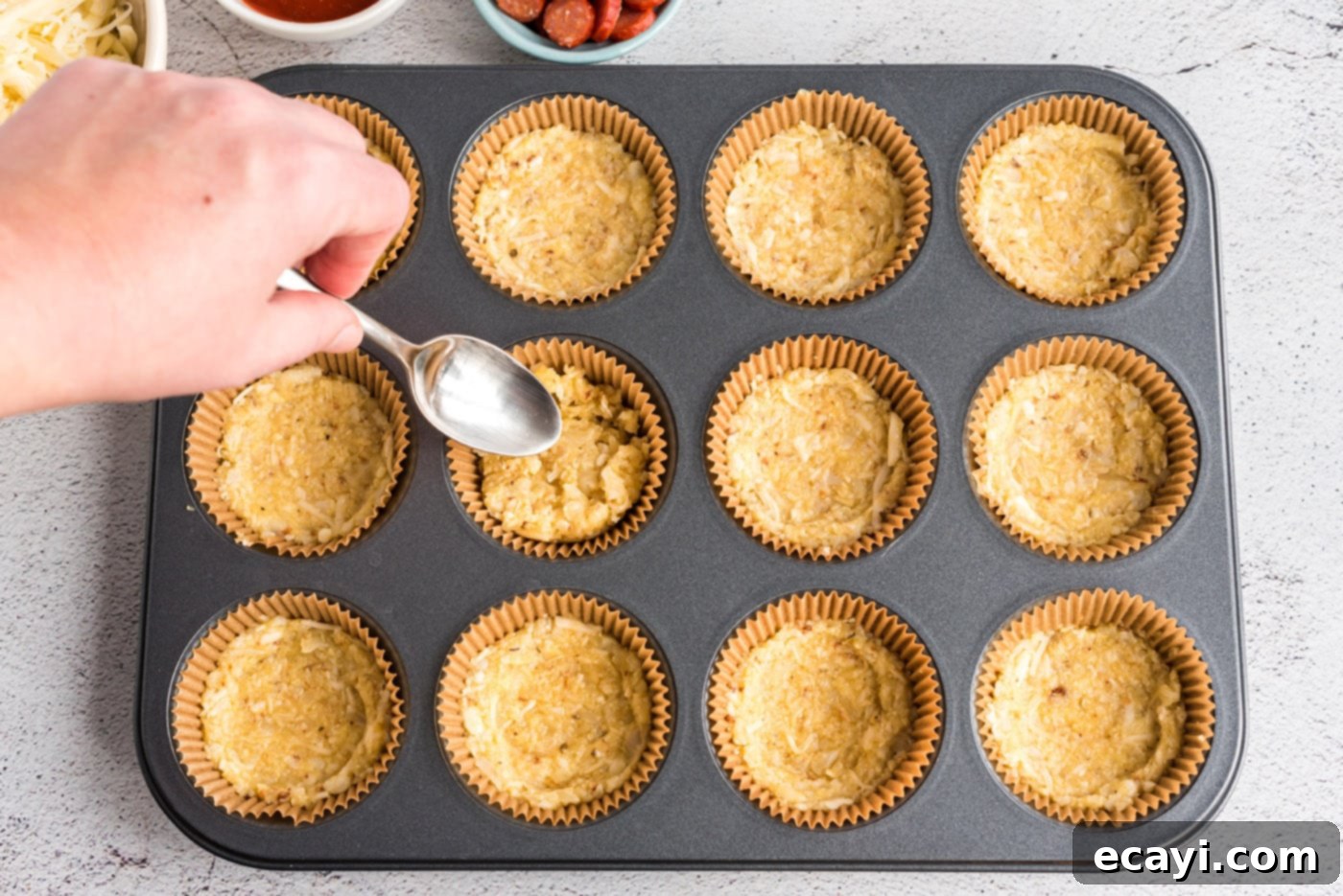 Cauliflower Crust Pizza Bites 6 flattening cauliflower crust mixture in a muffin tin with a spoon