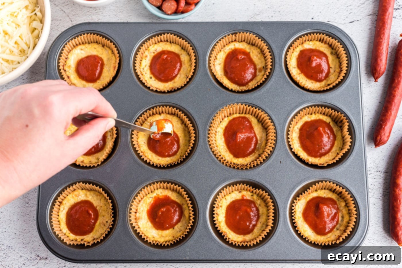 Cauliflower Crust Pizza Bites 7 spooning pizza sauce on top of cauliflower pizza bites in a muffin tin